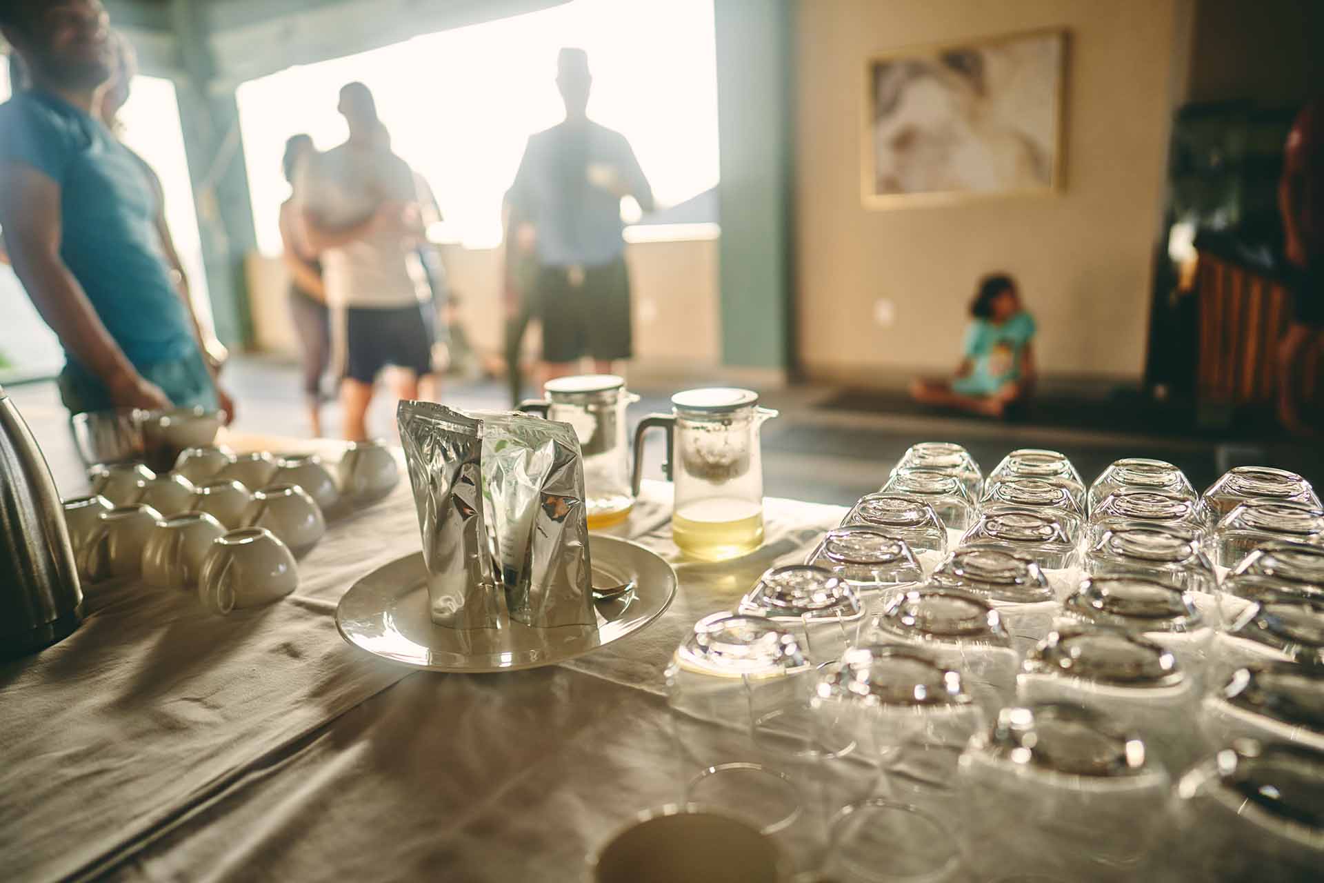 A table is set with cups, a pitcher, and beverage containers, while people mingle in the background.