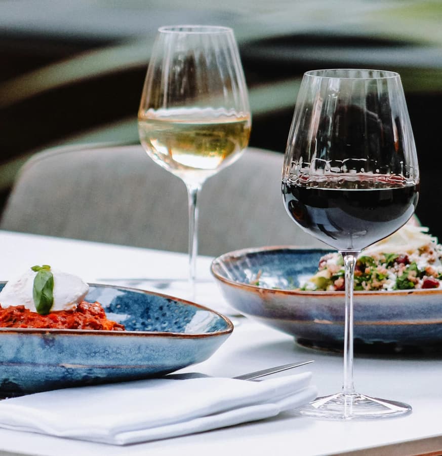 A table setting featuring a plate of pasta, a bowl of salad, and two glasses of wine.