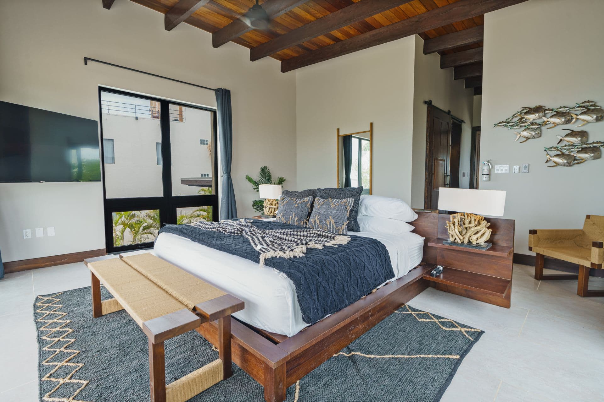 A modern bedroom with a wooden bed, decorative textiles, and large windows letting in natural light.
