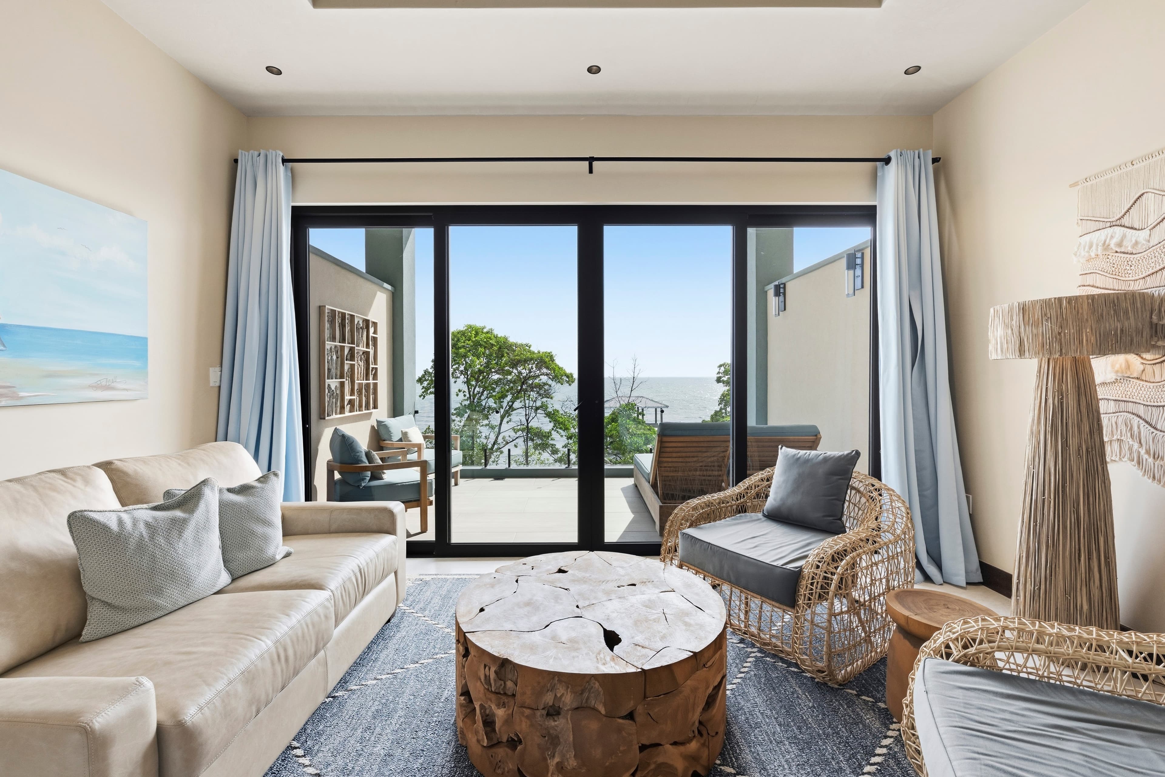 Cozy living room with a view of greenery and ocean beyond large glass doors.