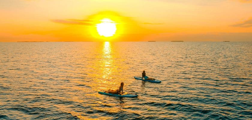 Two guests paddleboard on the Caribbean Sea during a golden sunrise near Prana Maya Island Resort.