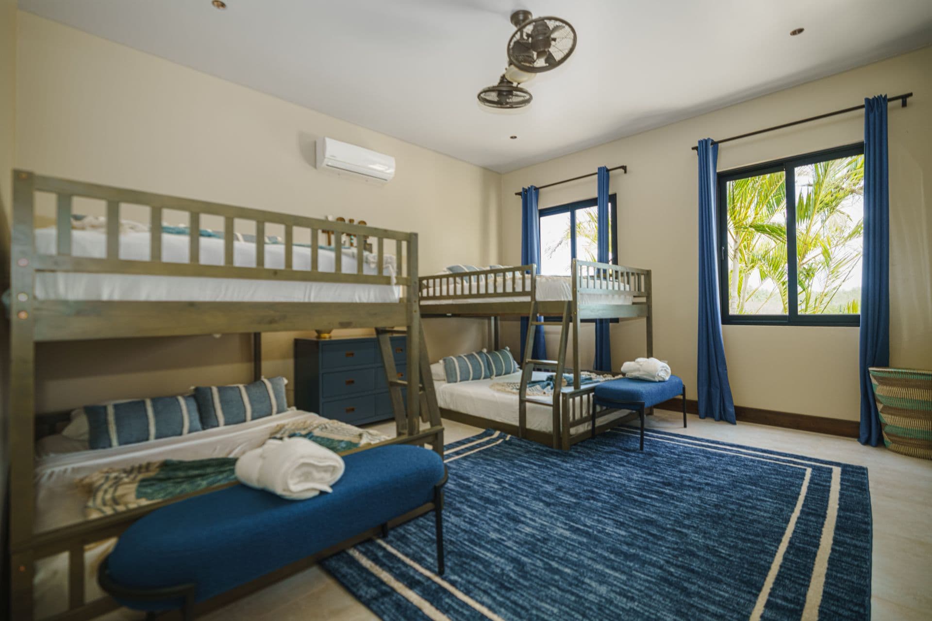 A bright, spacious bedroom featuring two sets of bunk beds and large windows with blue curtains.