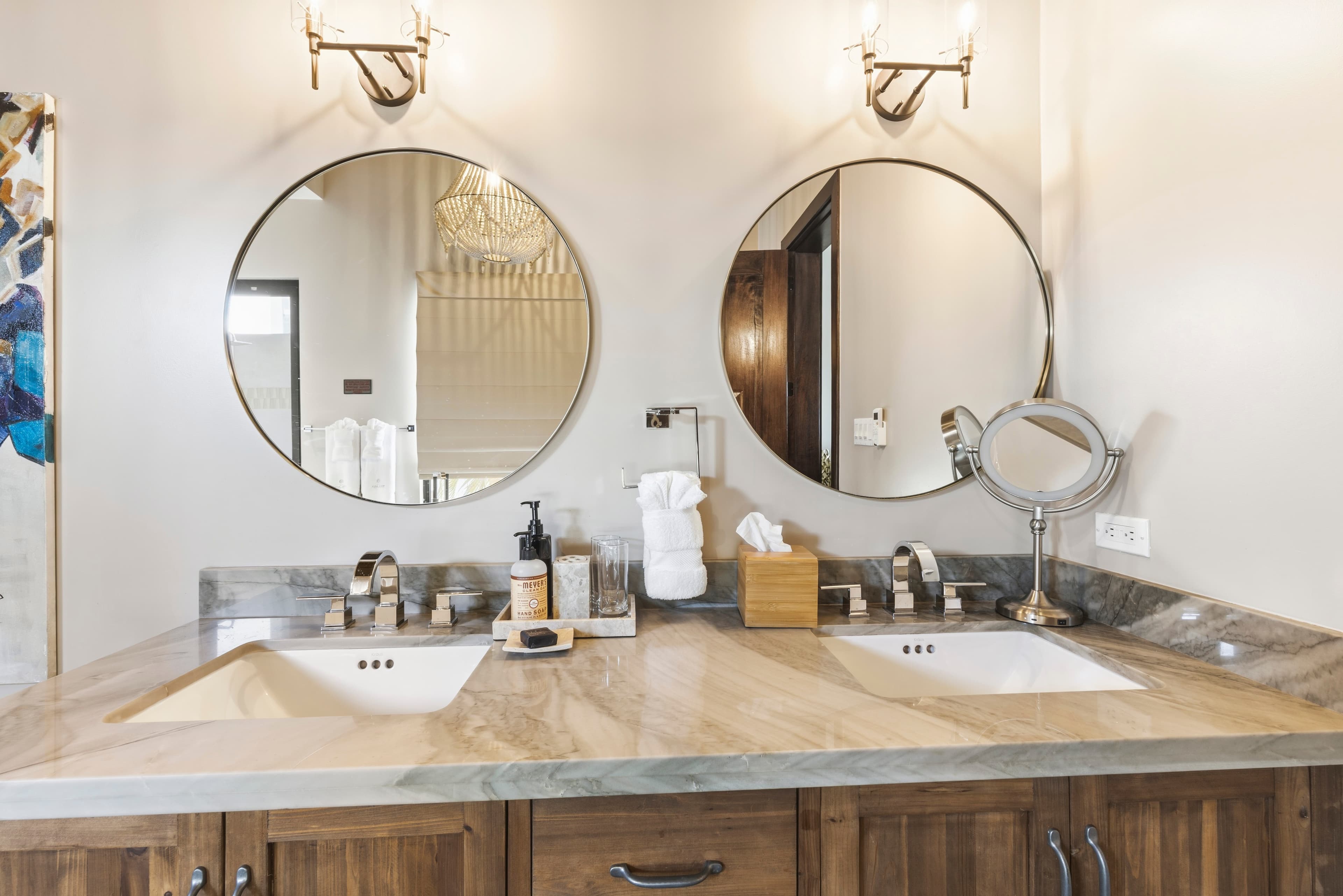 A modern bathroom with a double vanity, two round mirrors, and elegant lighting.
