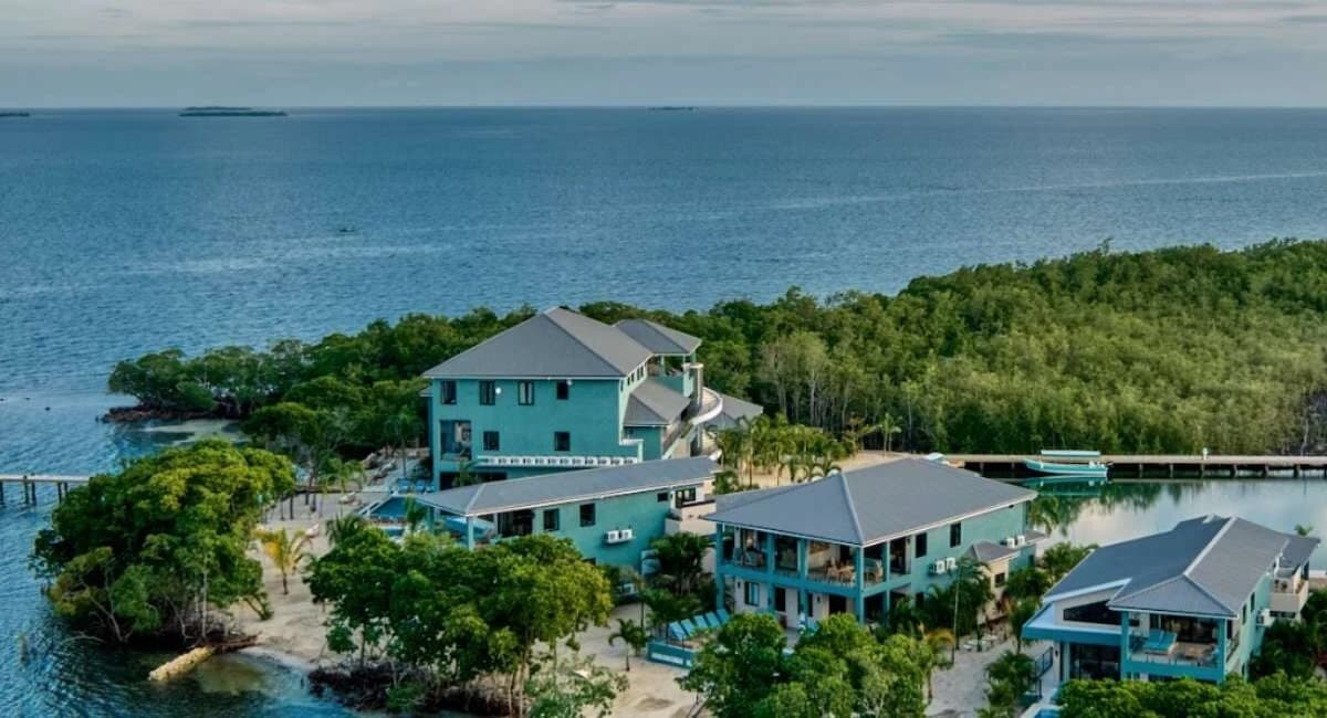 Aerial view of a turquoise coastal building complex surrounded by lush greenery and water.