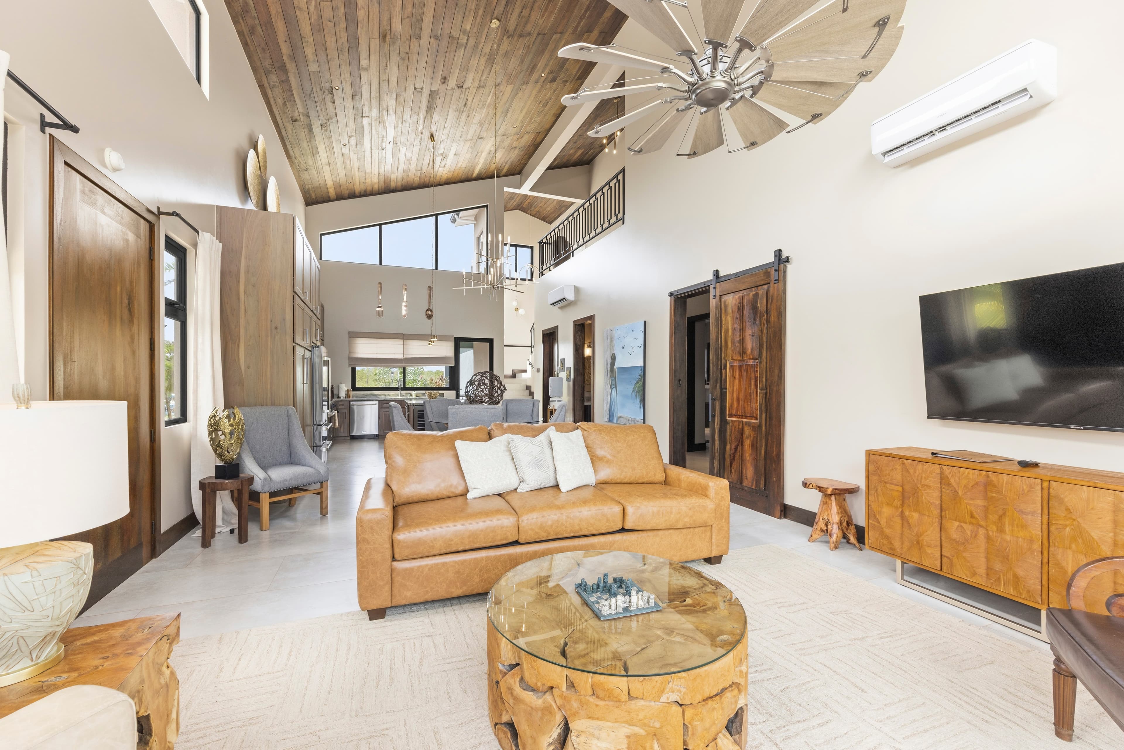 Spacious living room with a brown leather sofa, wooden accents, and large windows.