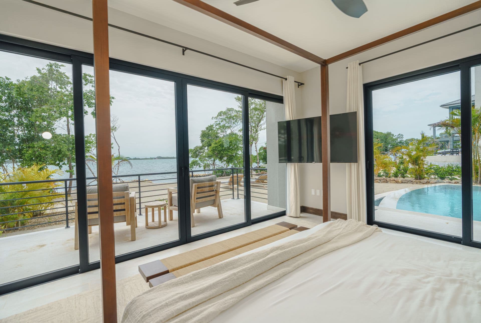 A modern bedroom with large windows showcasing a view of a lake and outdoor seating area.