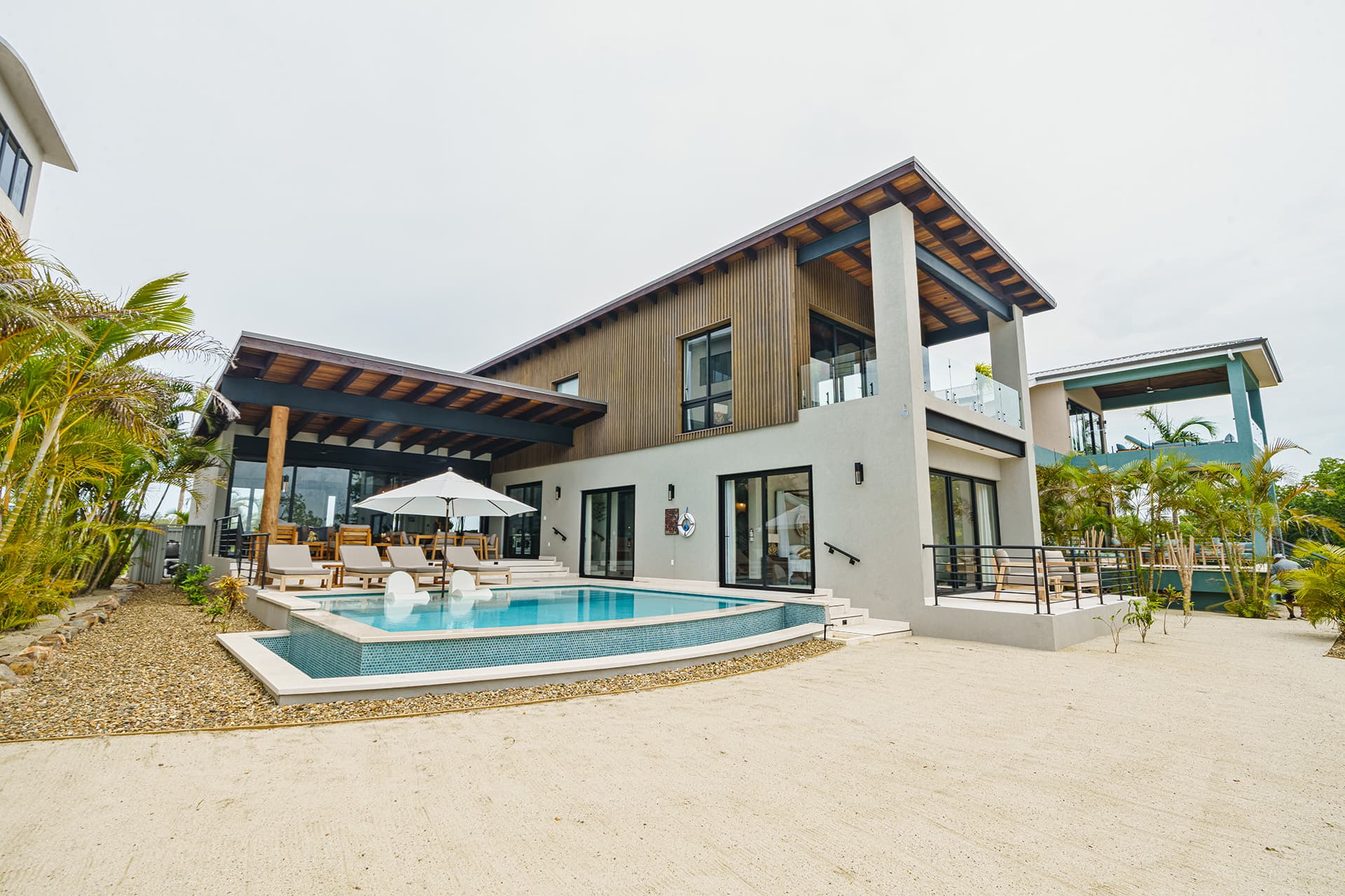 A modern two-story house with a pool and outdoor seating area, surrounded by tropical landscaping.