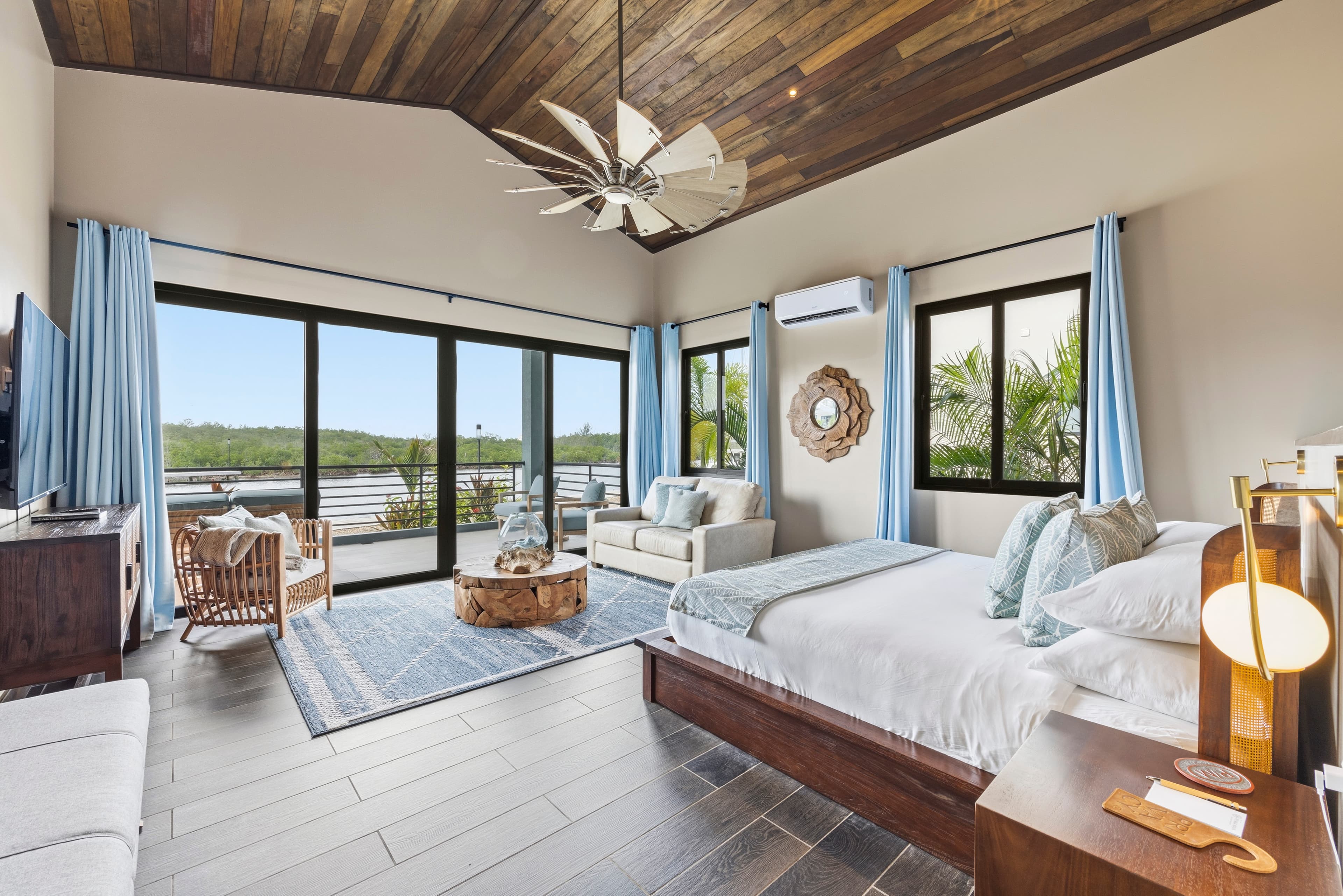 A spacious, modern bedroom with wooden accents, large windows, and a view of greenery.