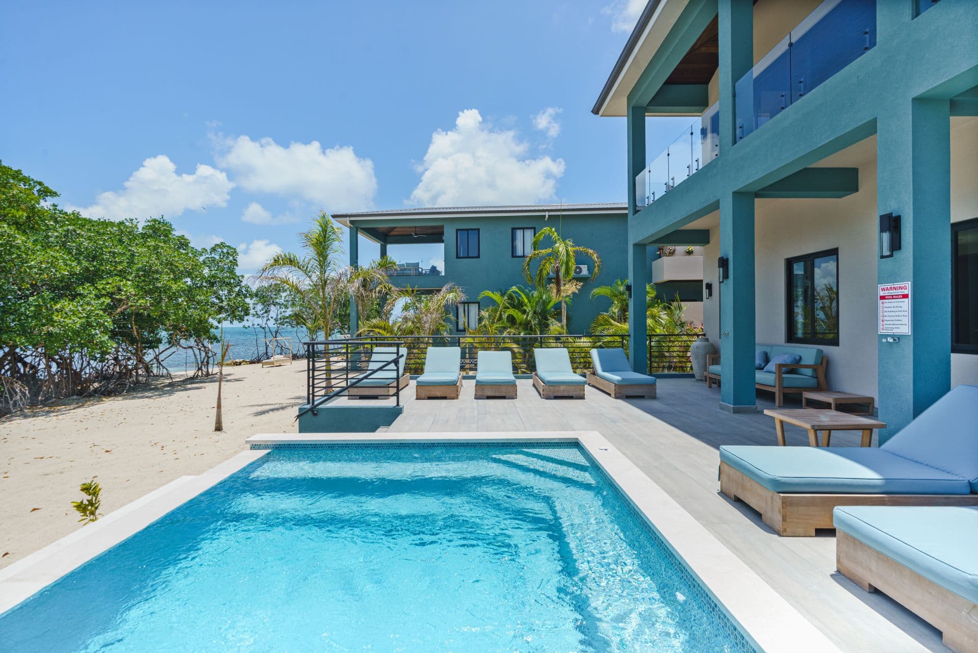 Modern beachfront villa with a swimming pool and lounging chairs surrounded by tropical greenery.