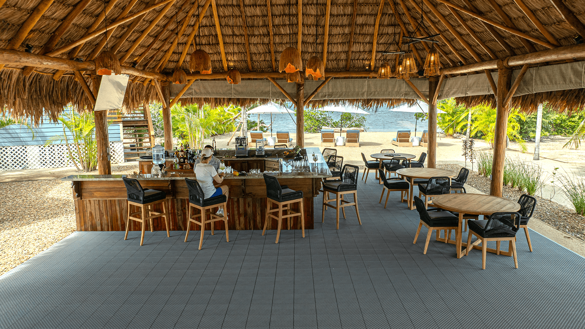A bartender prepares drinks at a rustic outdoor bar surrounded by tropical landscaping.