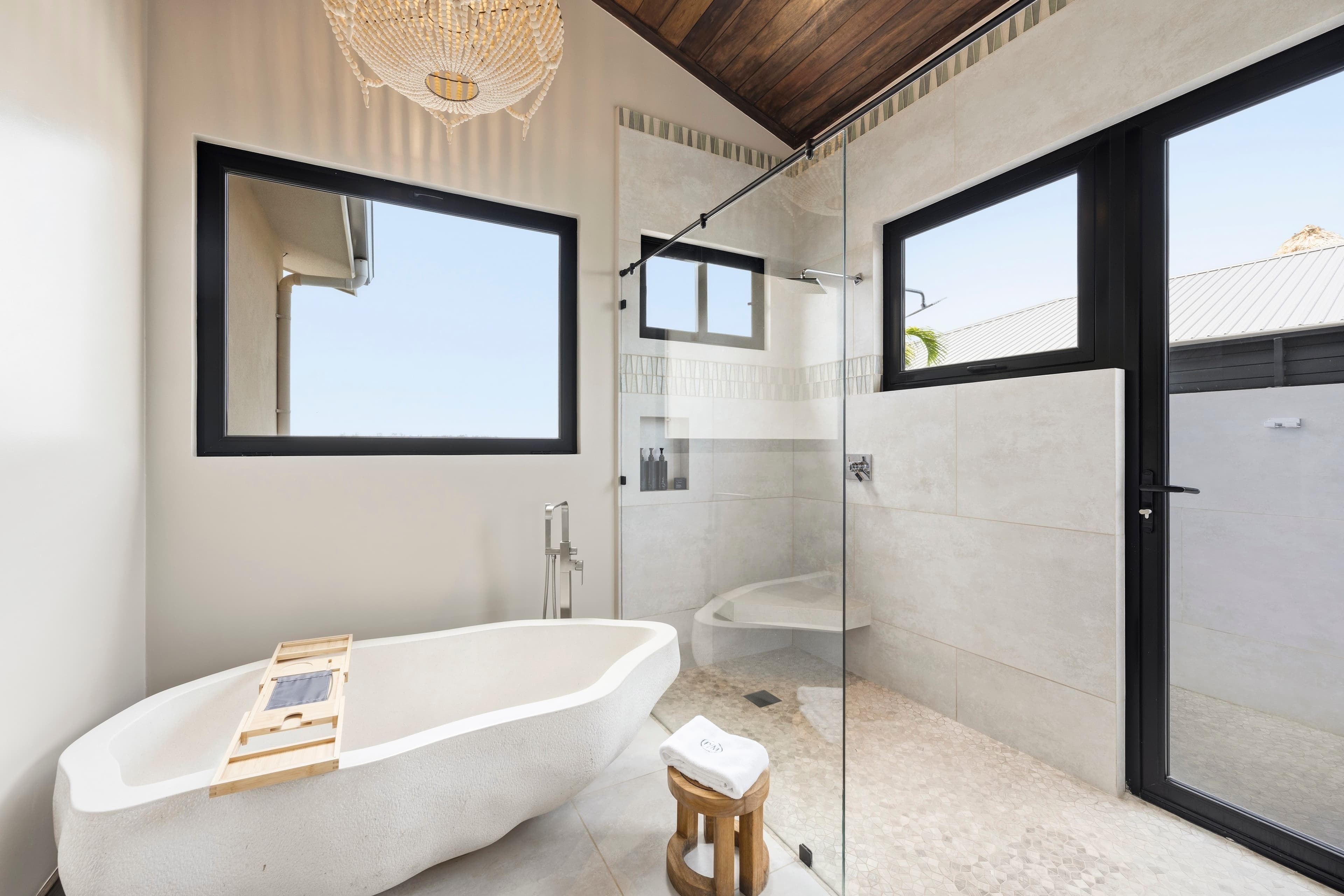 A modern bathroom featuring a freestanding bathtub, glass shower, and natural light from large windows.
