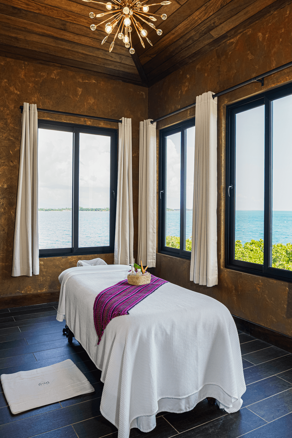 A serene spa room with a massage table and ocean views through large windows.