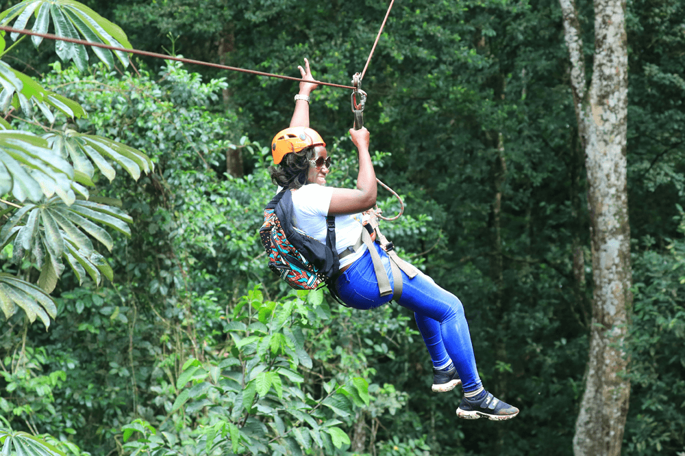 A person in a helmet zip lines through a lush green forest.