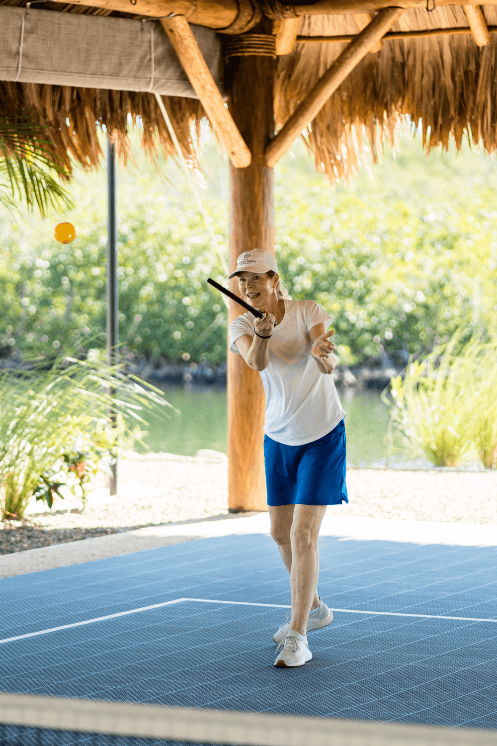 A player swings a paddle to hit a ball on an outdoor court near a scenic waterfront.