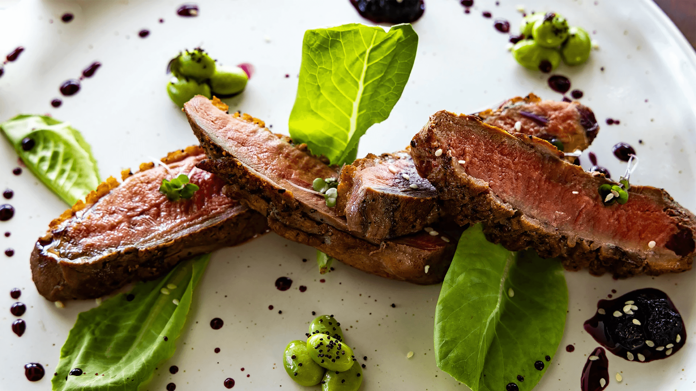 Sliced and plated steak garnished with greens and sauces.