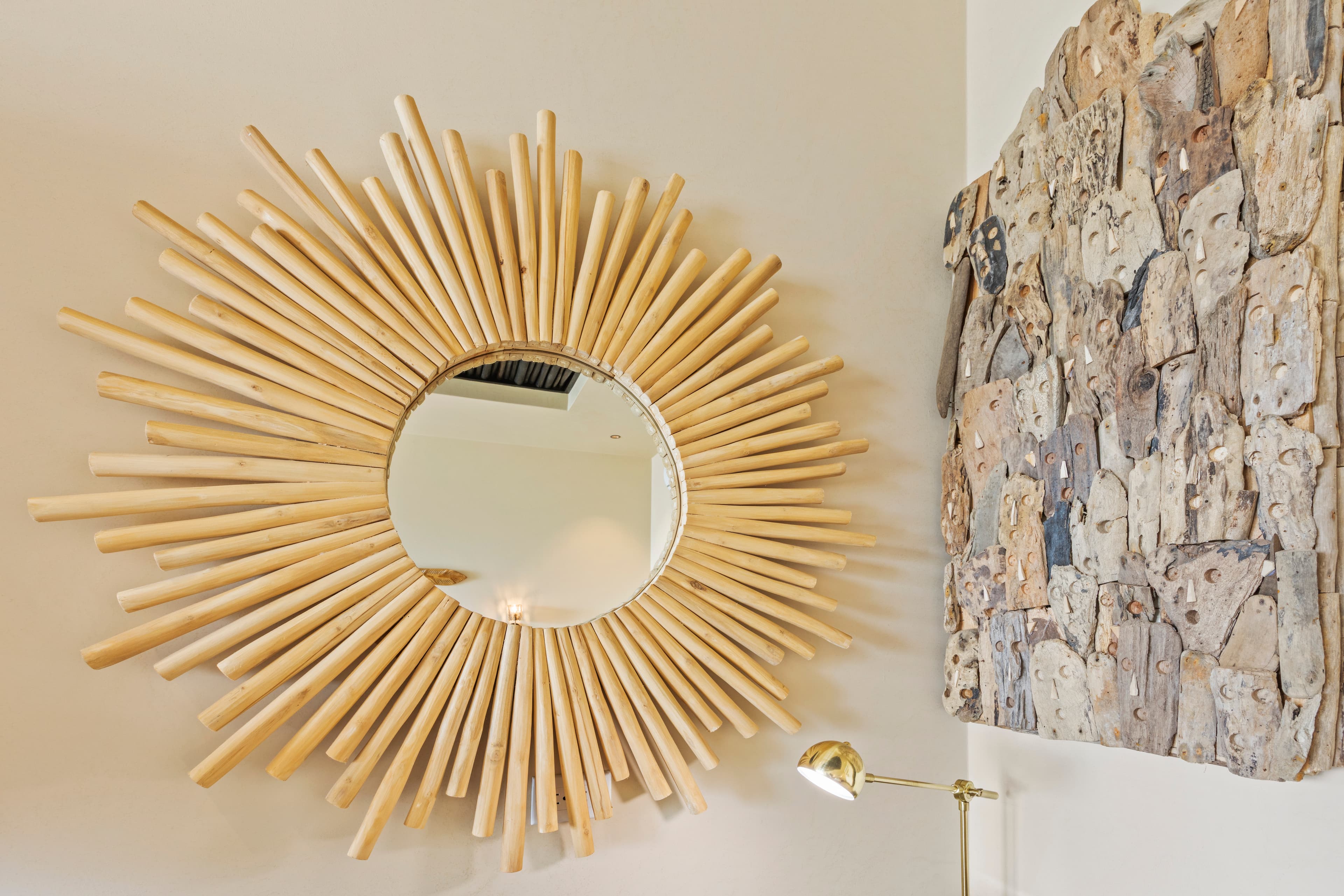 A circular mirror framed by sunburst-style wooden rays, next to a textured wall art piece.