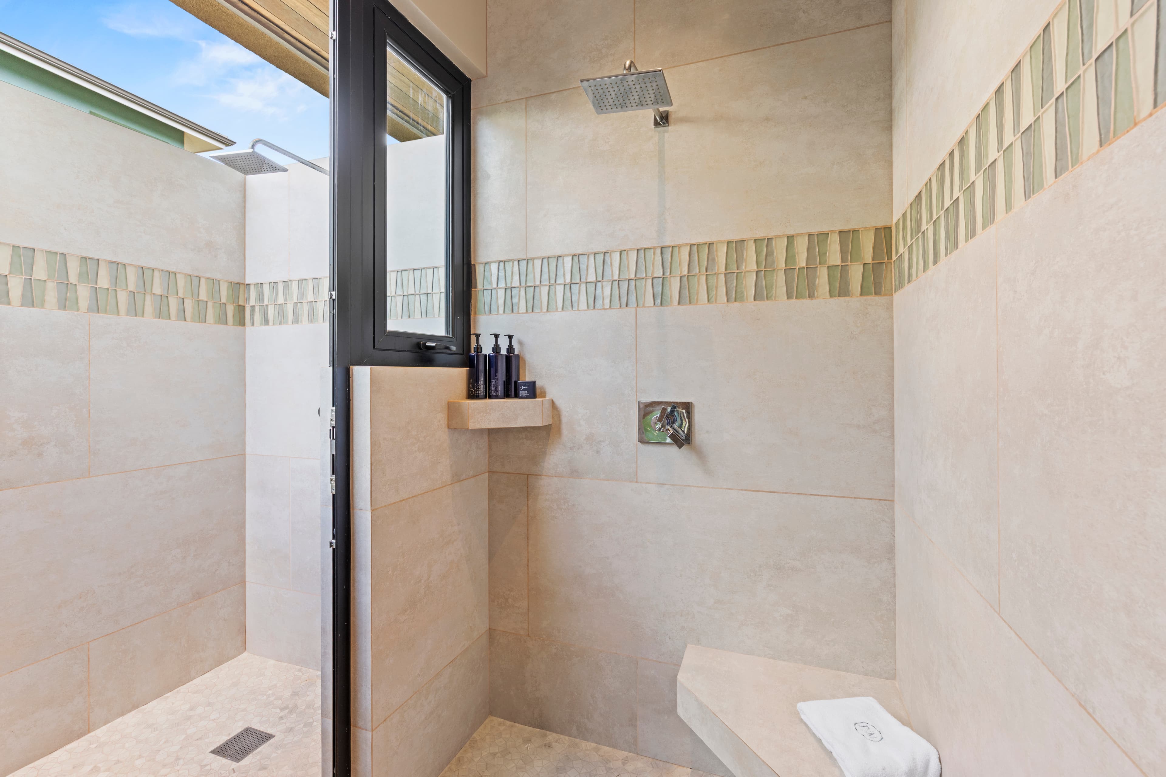 A modern shower with beige tiles, a rainfall showerhead, and a small shelf for toiletries.