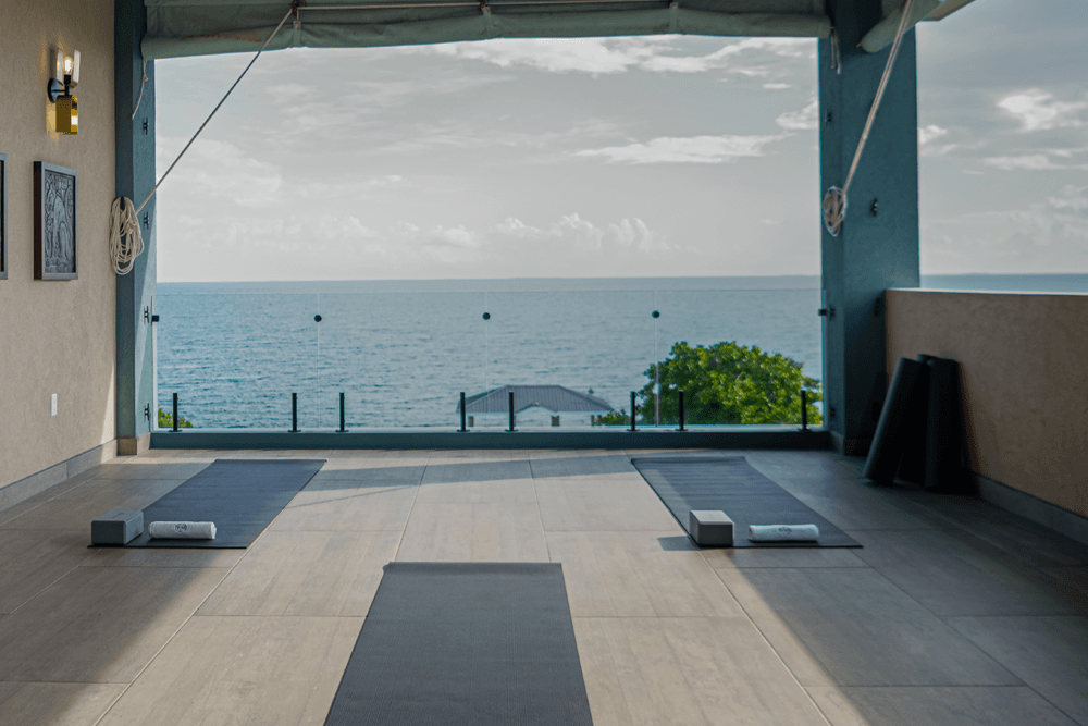 Two yoga mats and blocks are set up on a terrace overlooking the ocean.