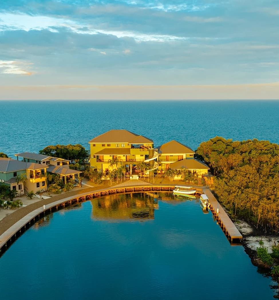 A waterfront property with multiple buildings surrounded by water and greenery, against a backdrop of the ocean.