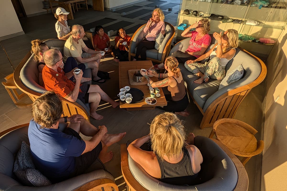 A diverse group of people gathers around a table in a cozy setting, engaged in conversation and enjoying drinks.