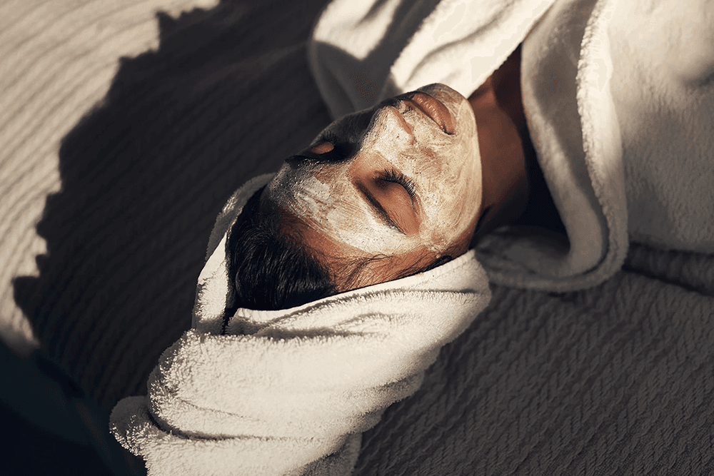 A person relaxing with a facial mask and a towel wrapped around their head.