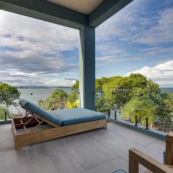 A blue lounge chair overlooks a serene waterfront view with lush trees and cloudy skies.