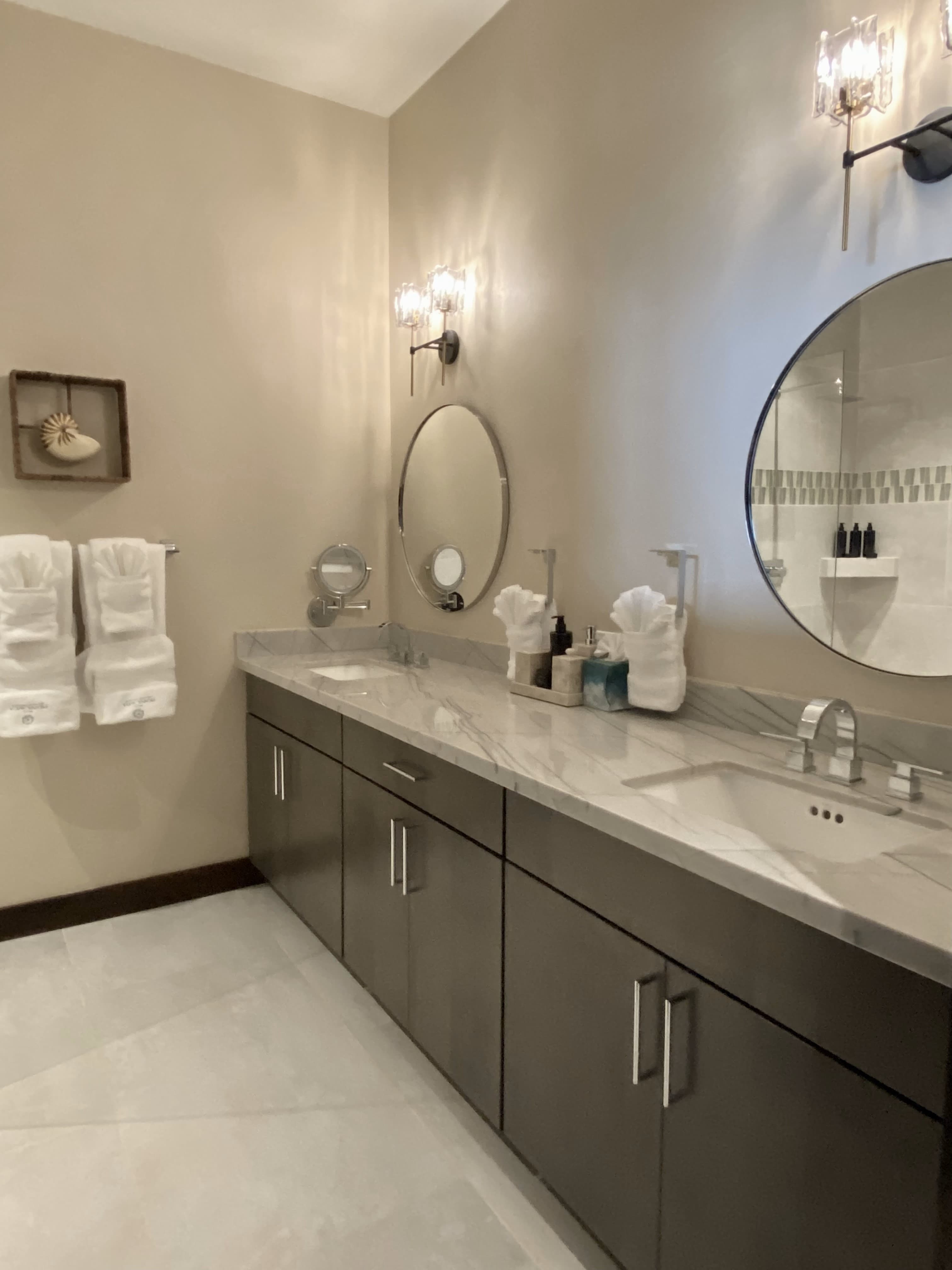 A modern bathroom featuring a marble countertop, round mirrors, and neatly arranged towels.
