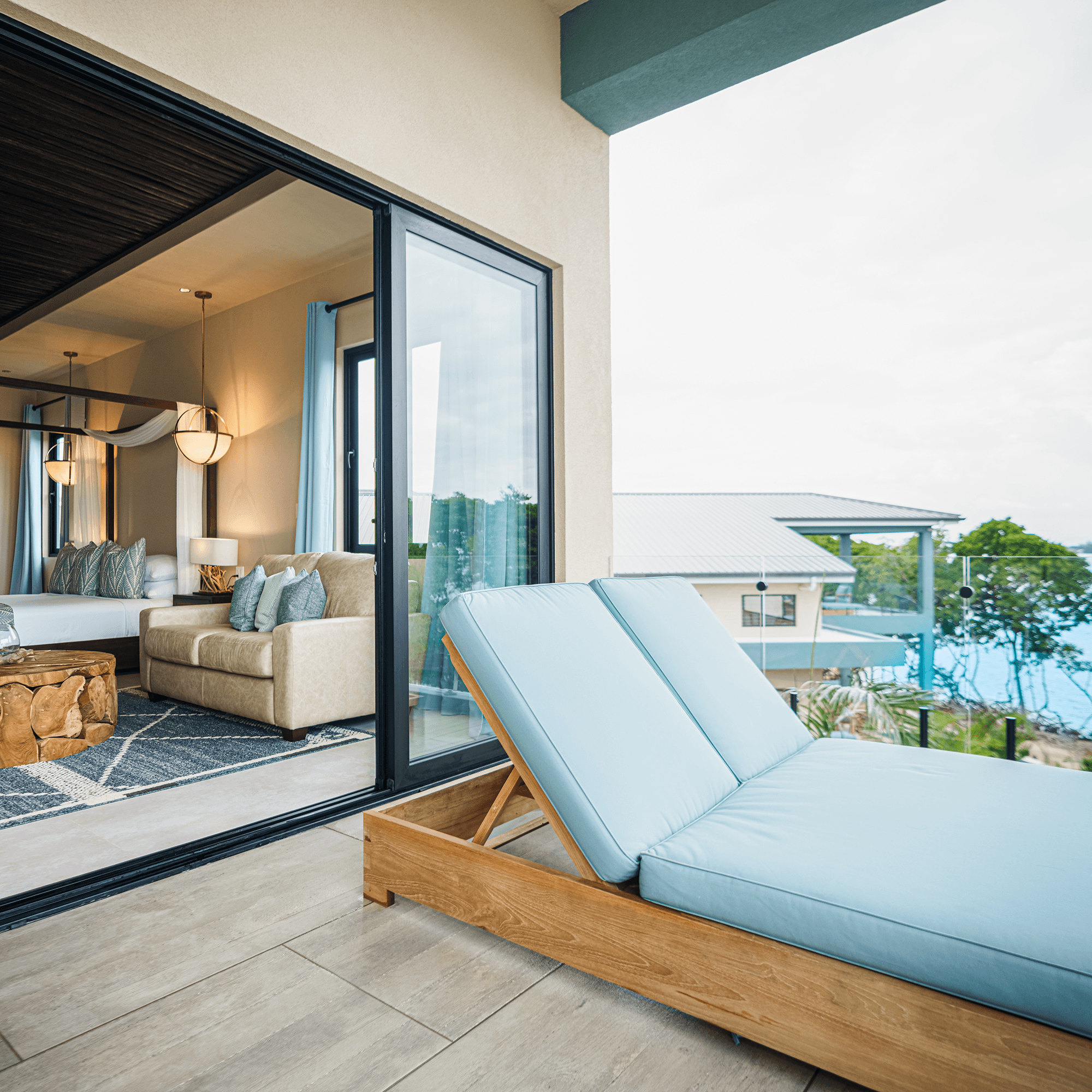 A sleek balcony with a blue lounge chair overlooks a cozy living area and scenic outdoor views.