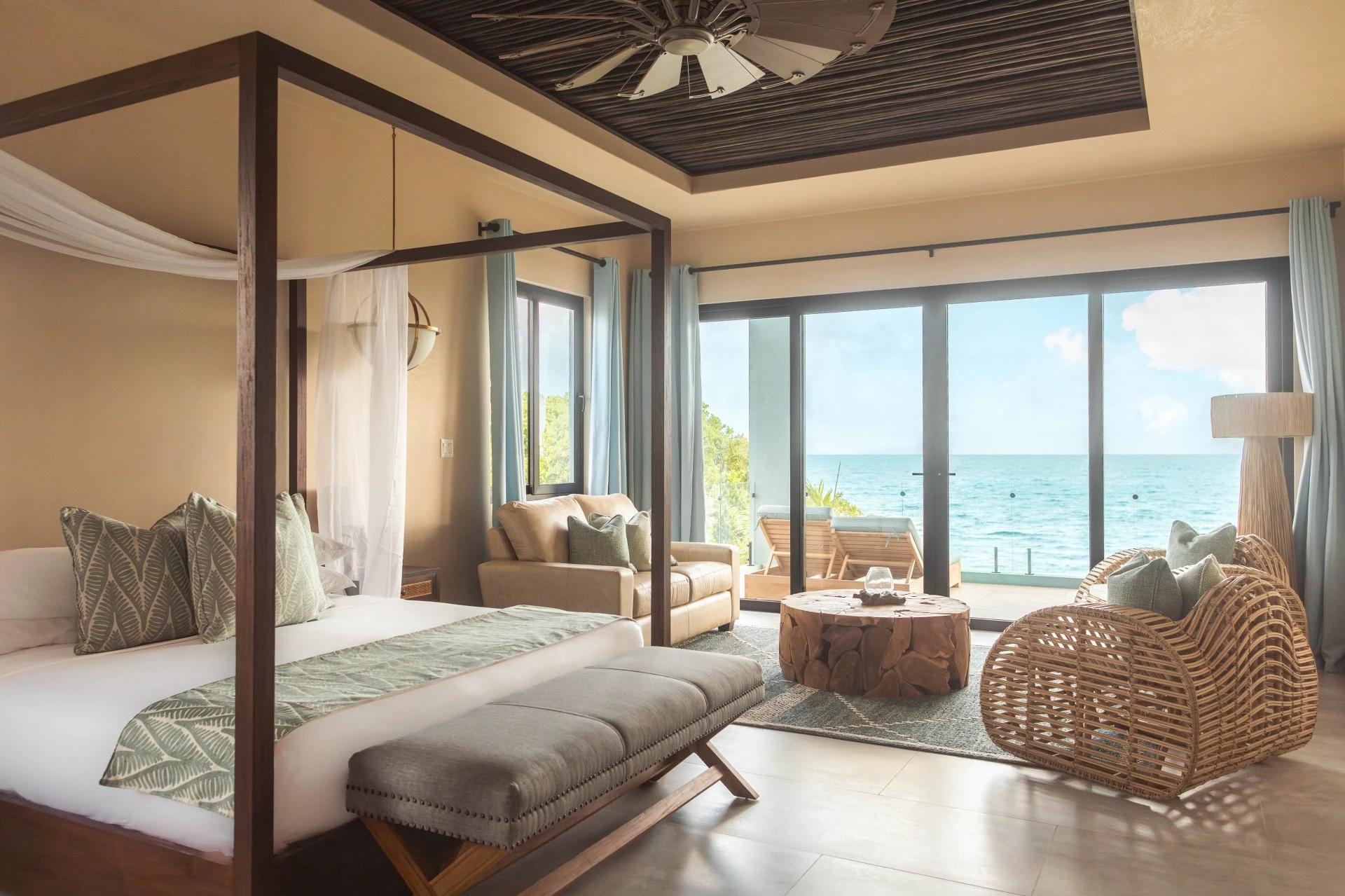 A luxurious bedroom with a four-poster bed, a cozy seating area, and ocean views through large windows.