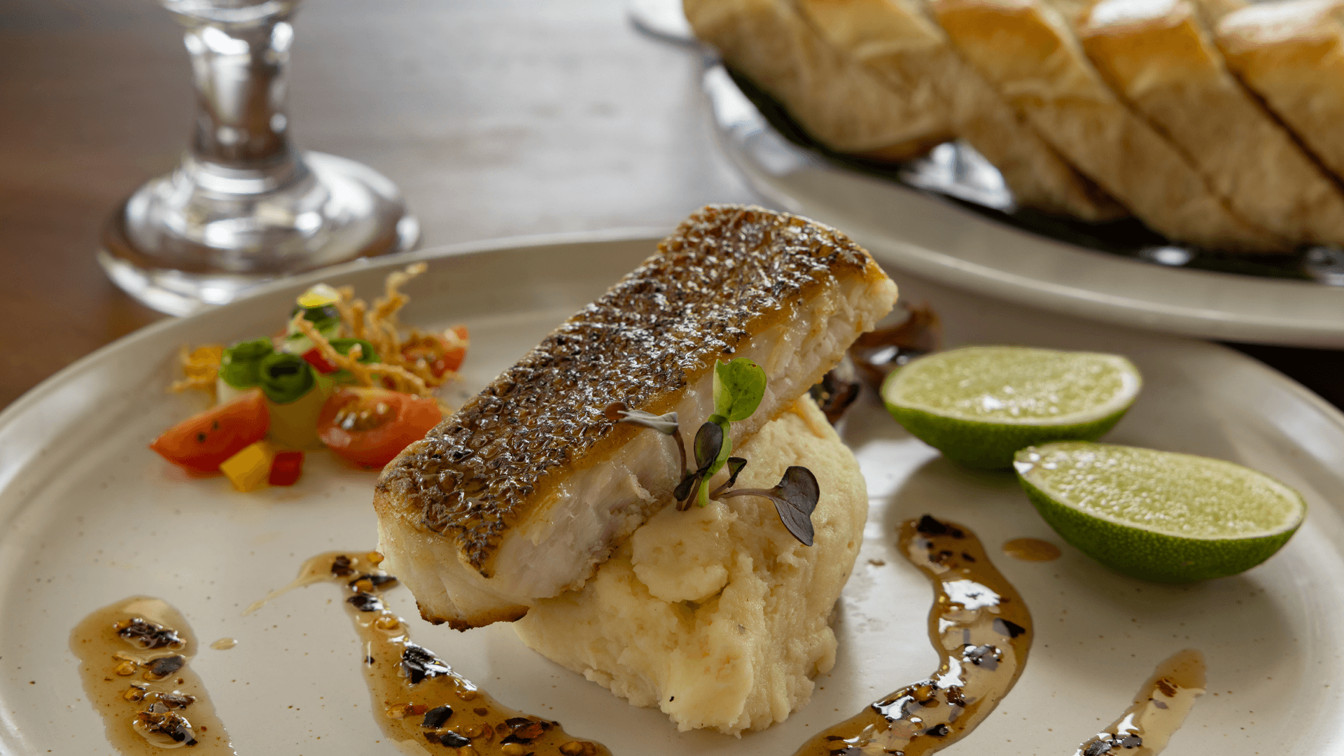 Pan-seared fish atop creamy mashed potatoes, garnished with lime and salad.