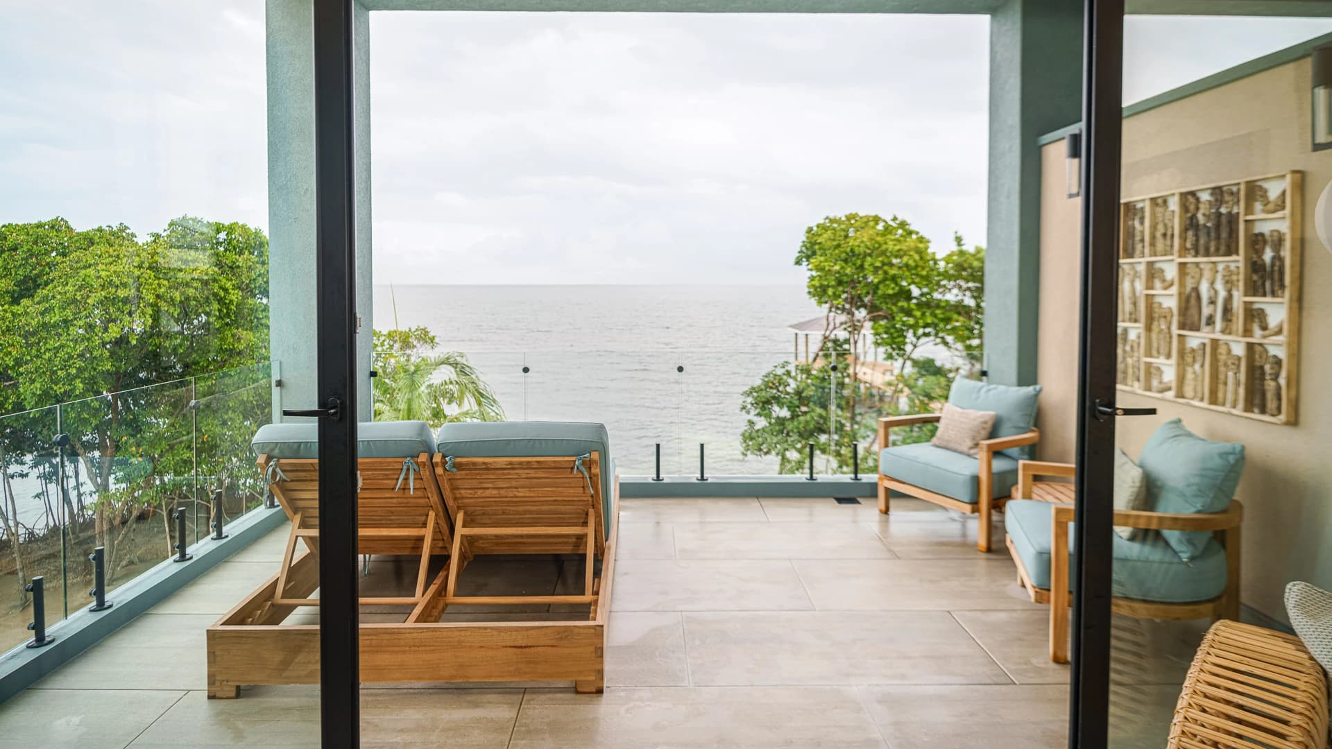 A spacious balcony with wooden furniture overlooks a tranquil sea view surrounded by greenery.