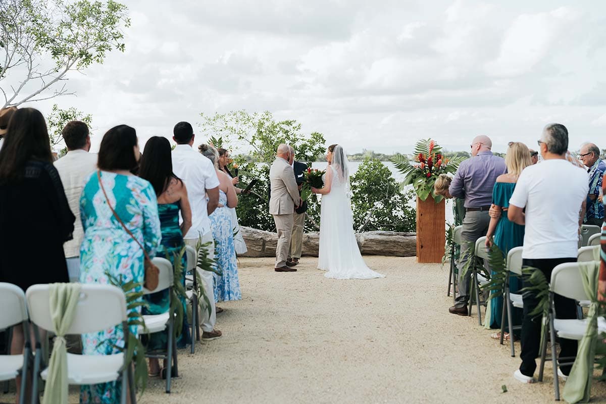 A bride and groom stand at an outdoor altar surrounded by guests during a wedding ceremony.