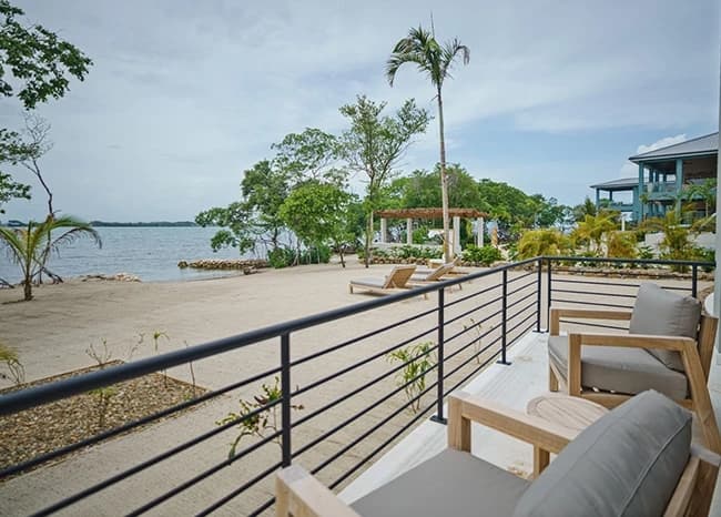 Seating area overlooking a sandy beach and lush greenery by a calm body of water.