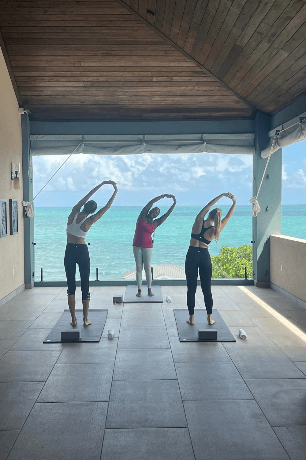 Three people practicing yoga on mats in a bright, open space overlooking the ocean.
