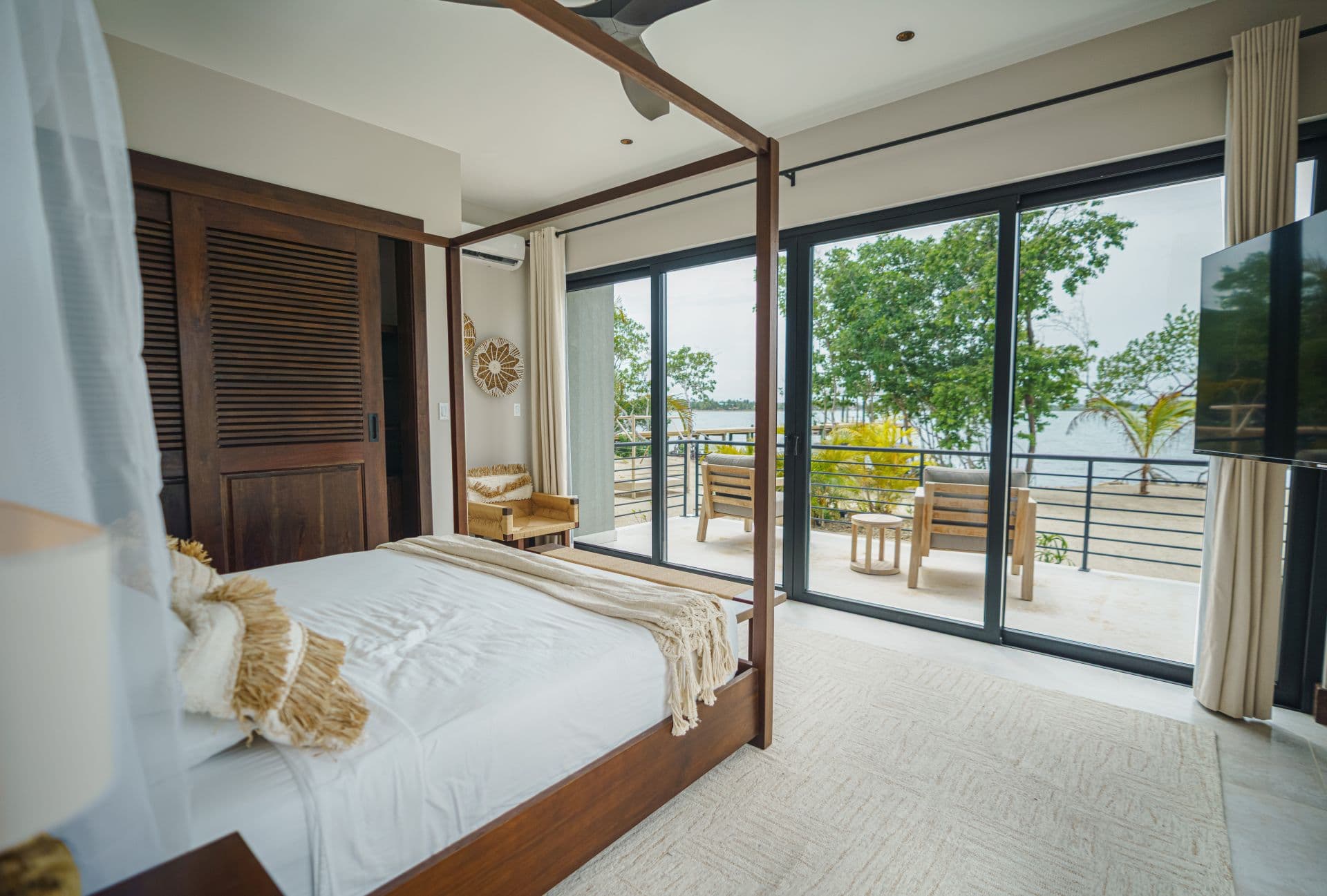 A modern bedroom with a four-poster bed and large glass doors opening to a lakeside view.