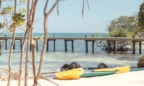 Kayaks on a sandy beach with a wooden pier extending over calm blue waters.