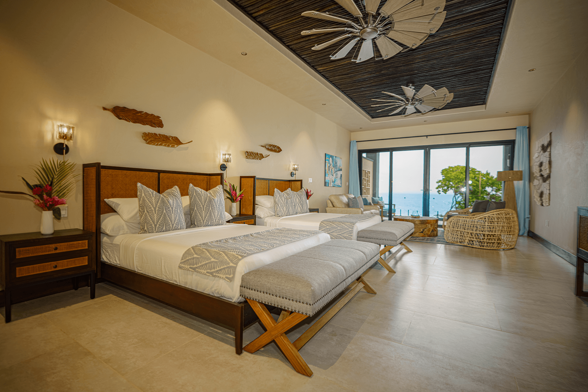 A spacious, modern hotel room featuring two beds, tropical decor, and large windows overlooking the ocean.