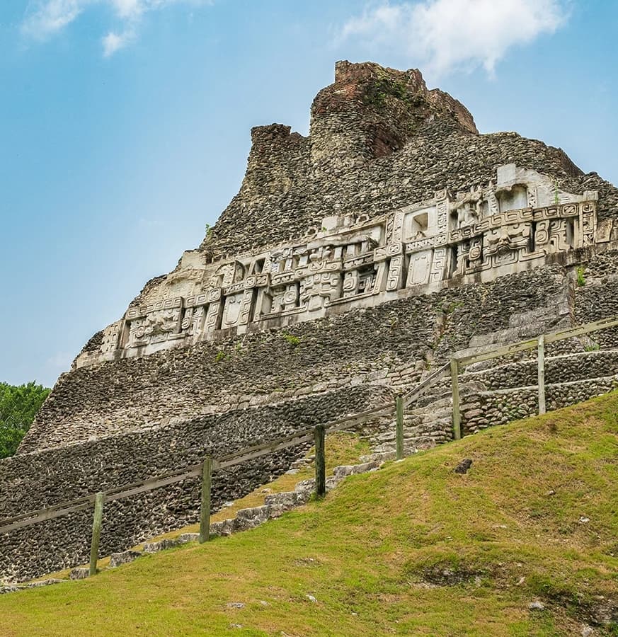 Ancient stone structure adorned with carvings, set against a blue sky and grassy landscape.