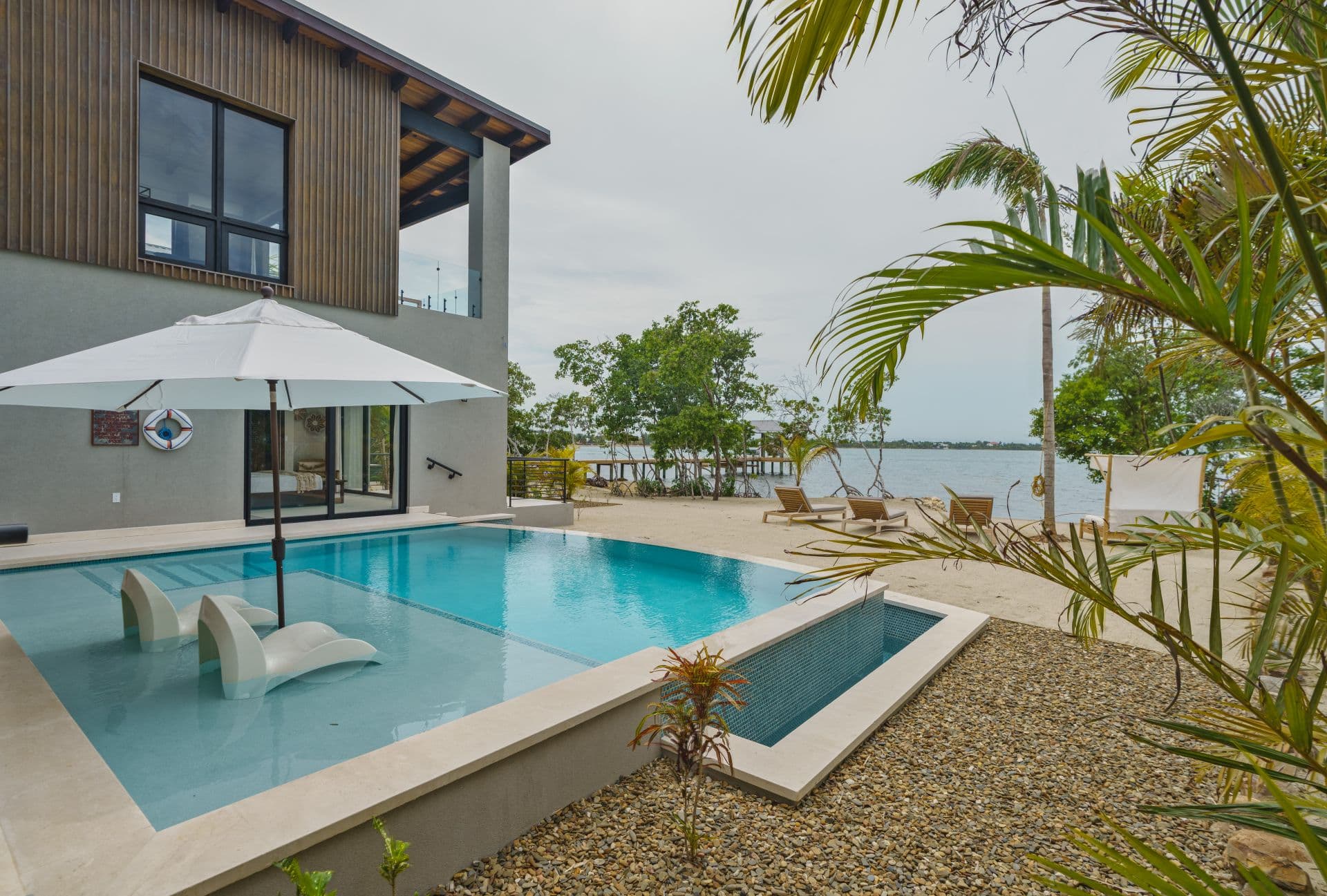 A modern home features a swimming pool and outdoor lounging area by the water.