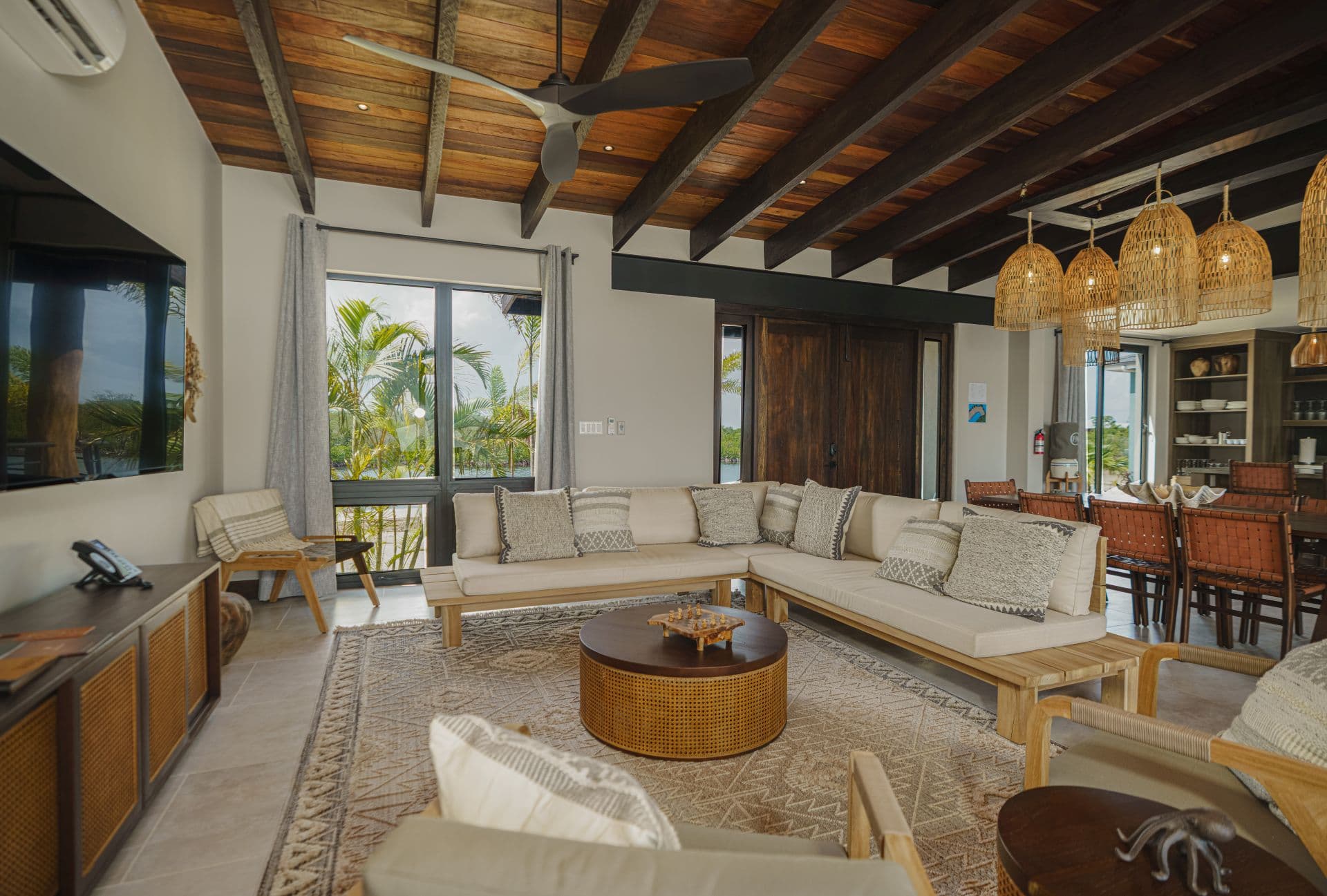 A modern living room featuring a wooden ceiling, cozy seating, and large windows with views of greenery.