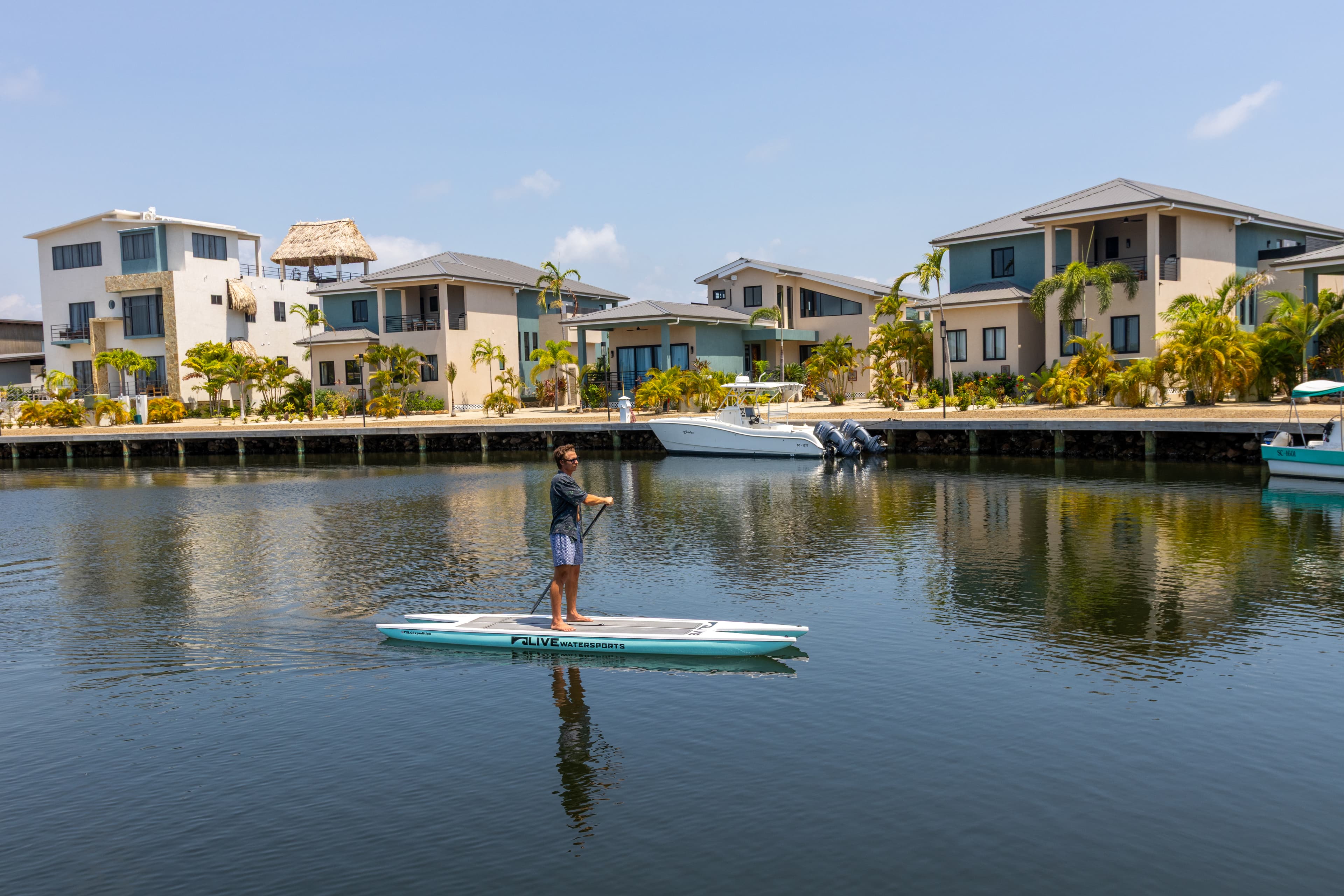 A person paddleboards on a calm waterway surrounded by modern houses.