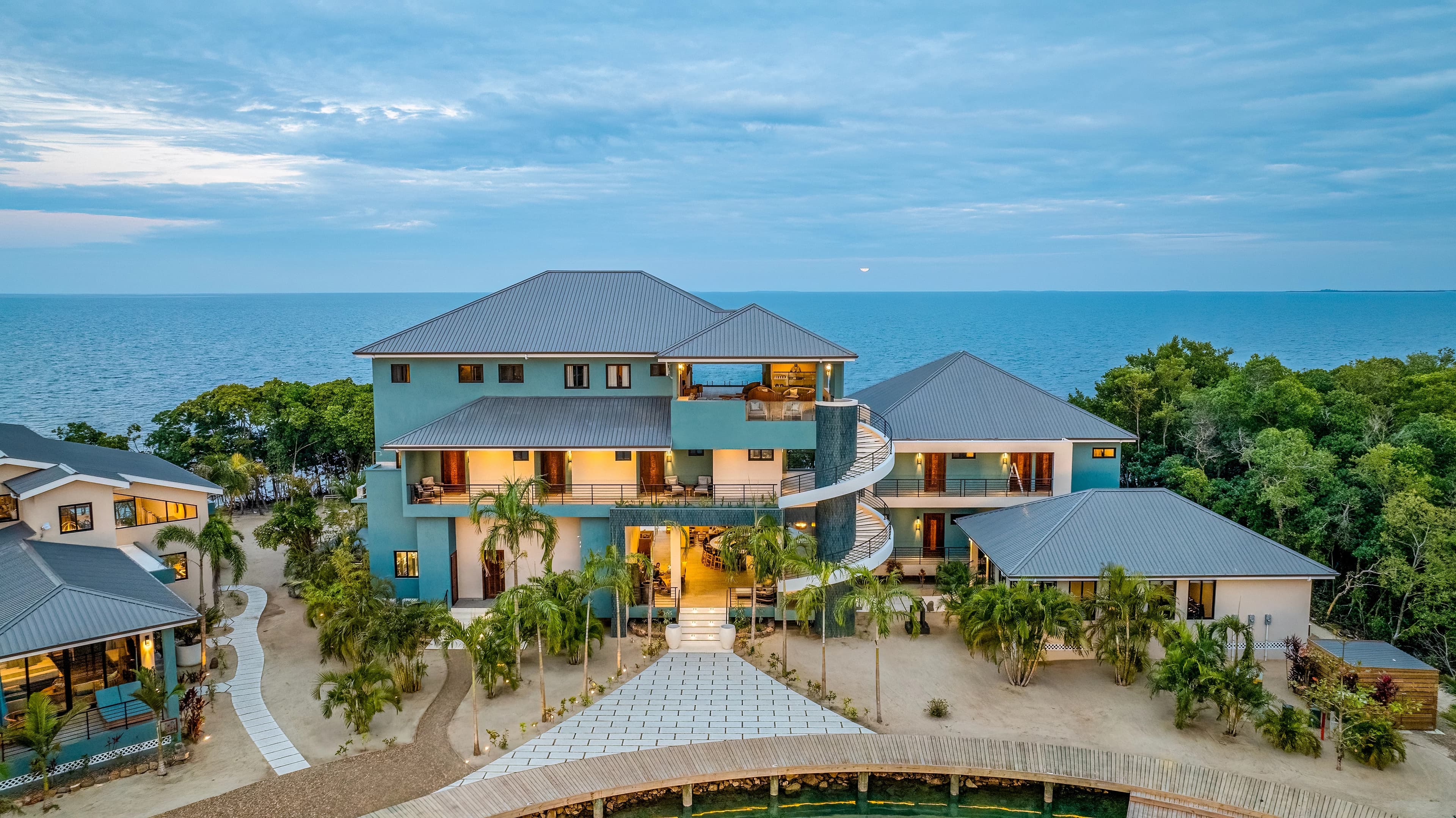 A modern seaside villa with a spiral staircase, surrounded by lush greenery and ocean views.