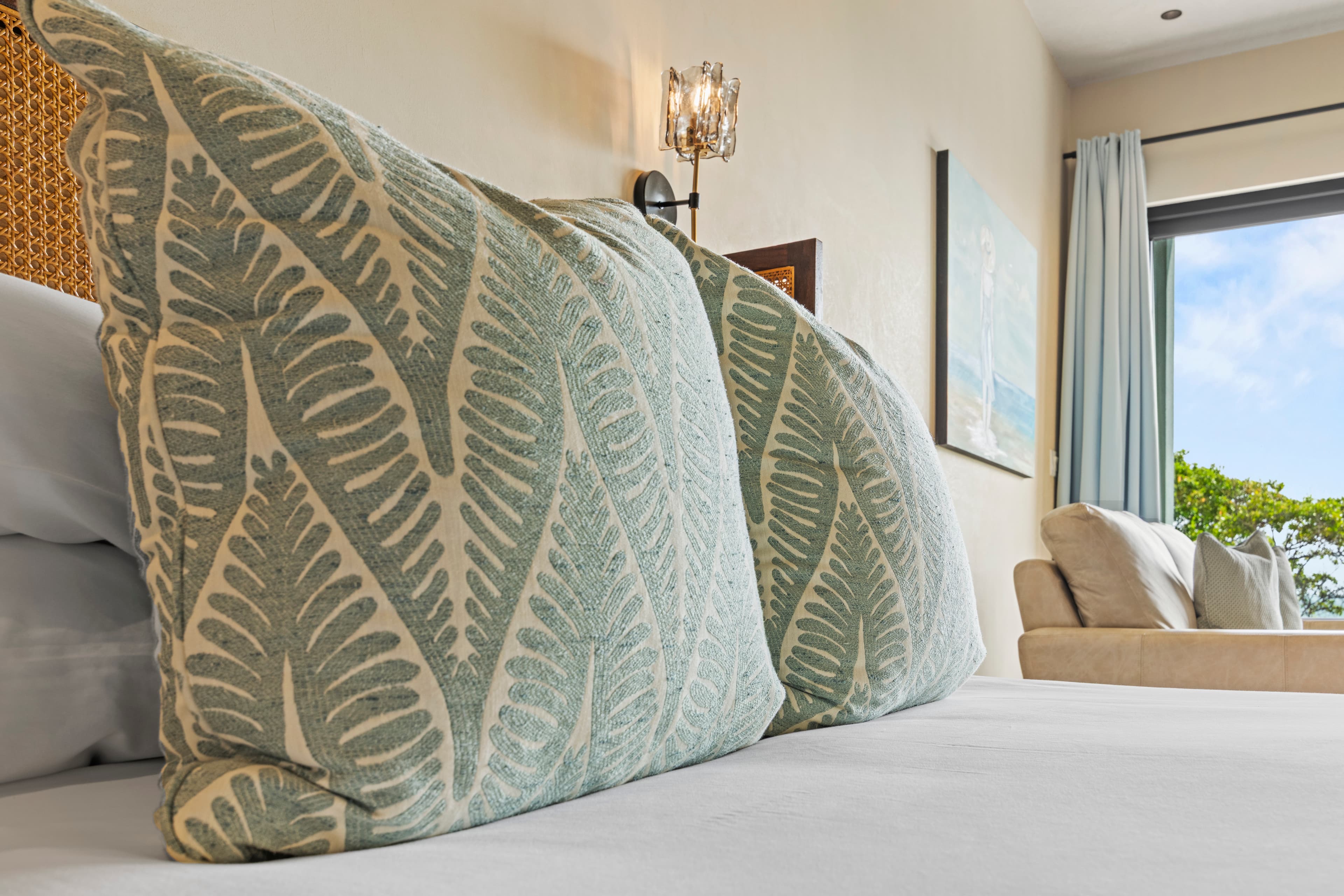 Close-up of decorative pillows with a fern pattern on a bed in a bright, airy room.