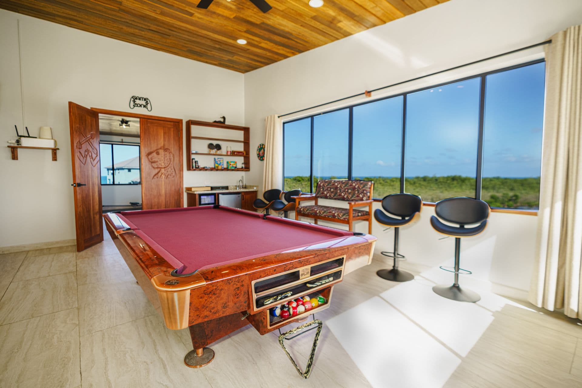 A bright game room featuring a pool table, seating area, and large windows with a view.