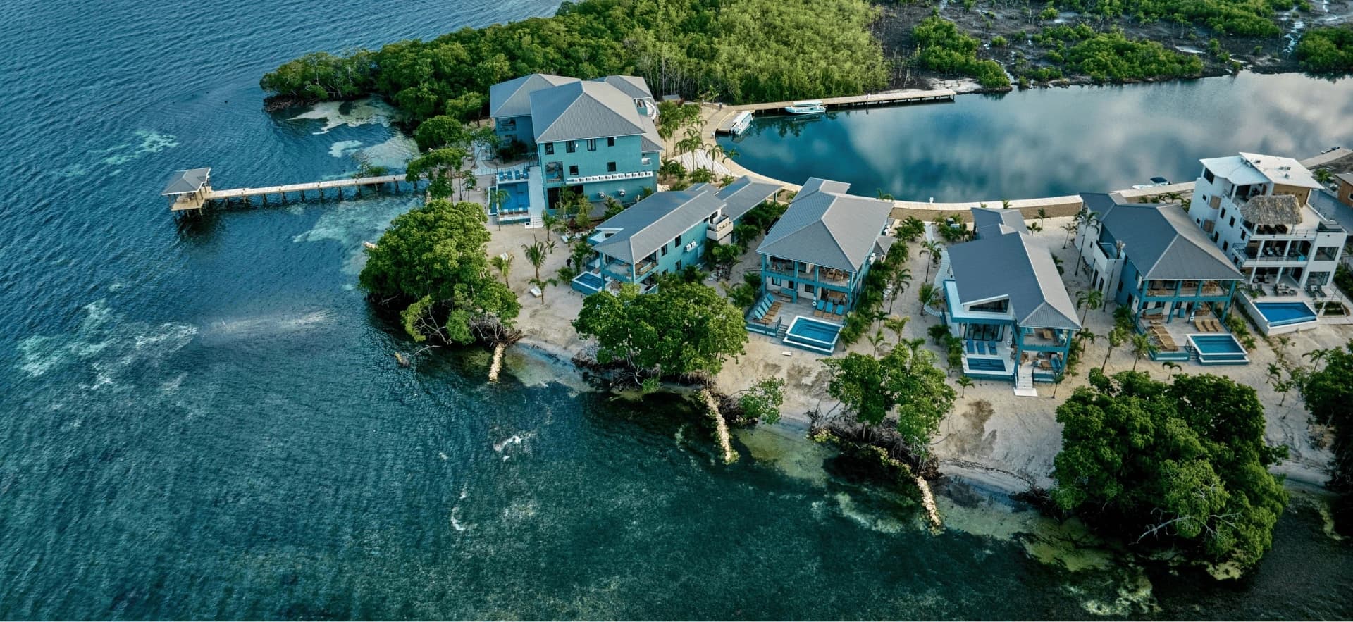 Aerial view of a coastal property with multiple modern houses surrounded by water and greenery.