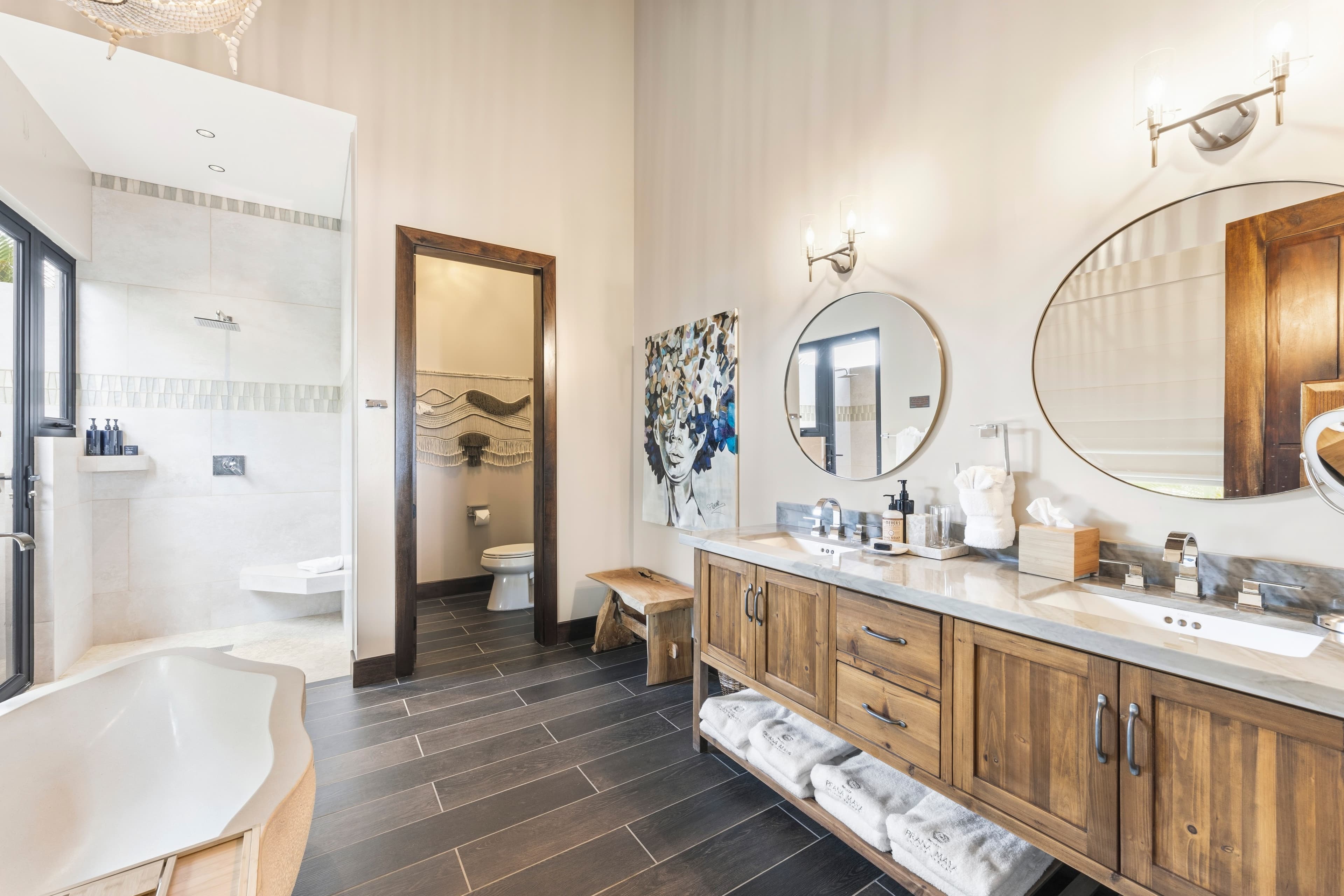Modern bathroom featuring a wooden vanity, circular mirrors, a freestanding tub, and a walk-in shower.