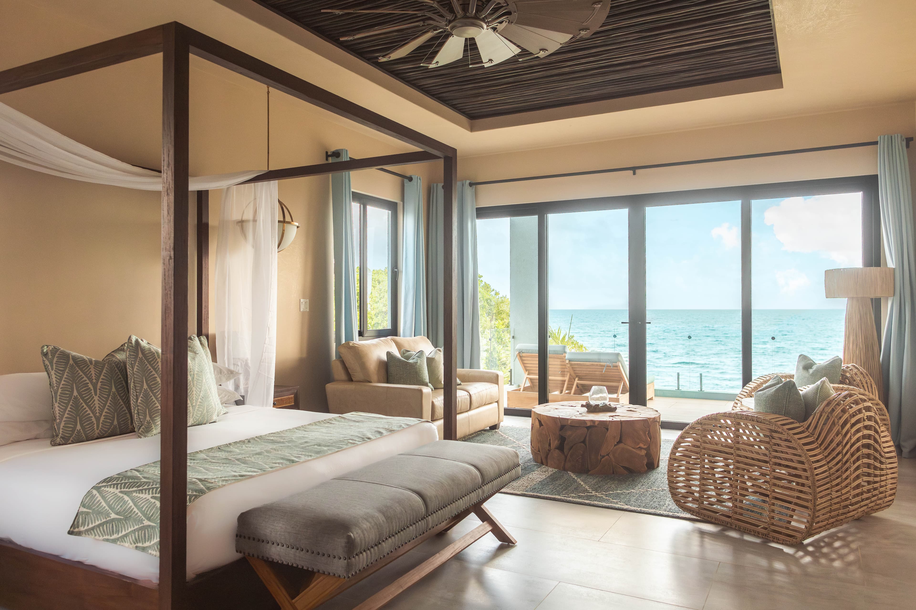 A luxurious bedroom with a partial canopy bed, a seating area, and large windows overlooking the ocean.