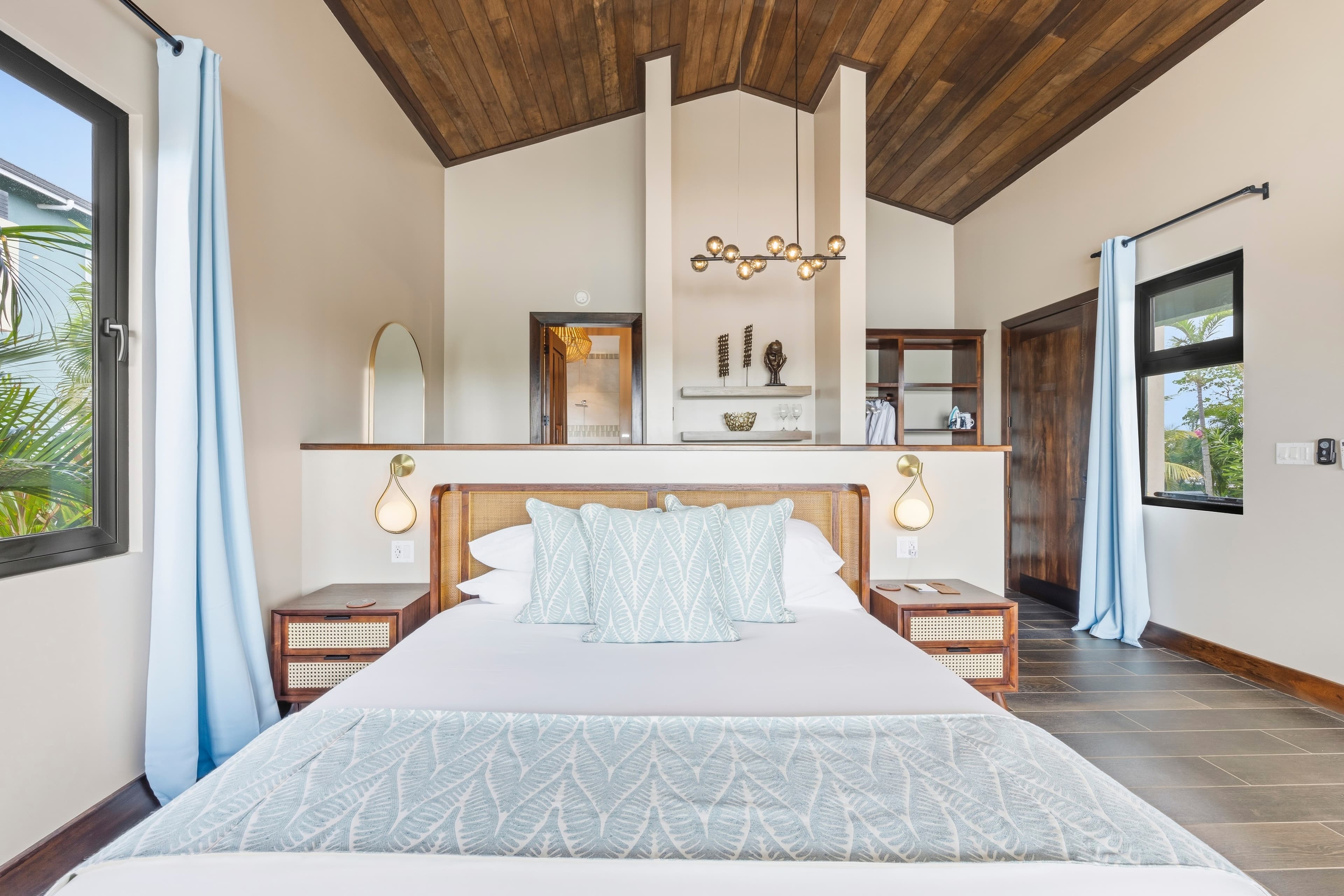 A modern bedroom featuring a bed with decorative pillows, wooden accents, and large windows.