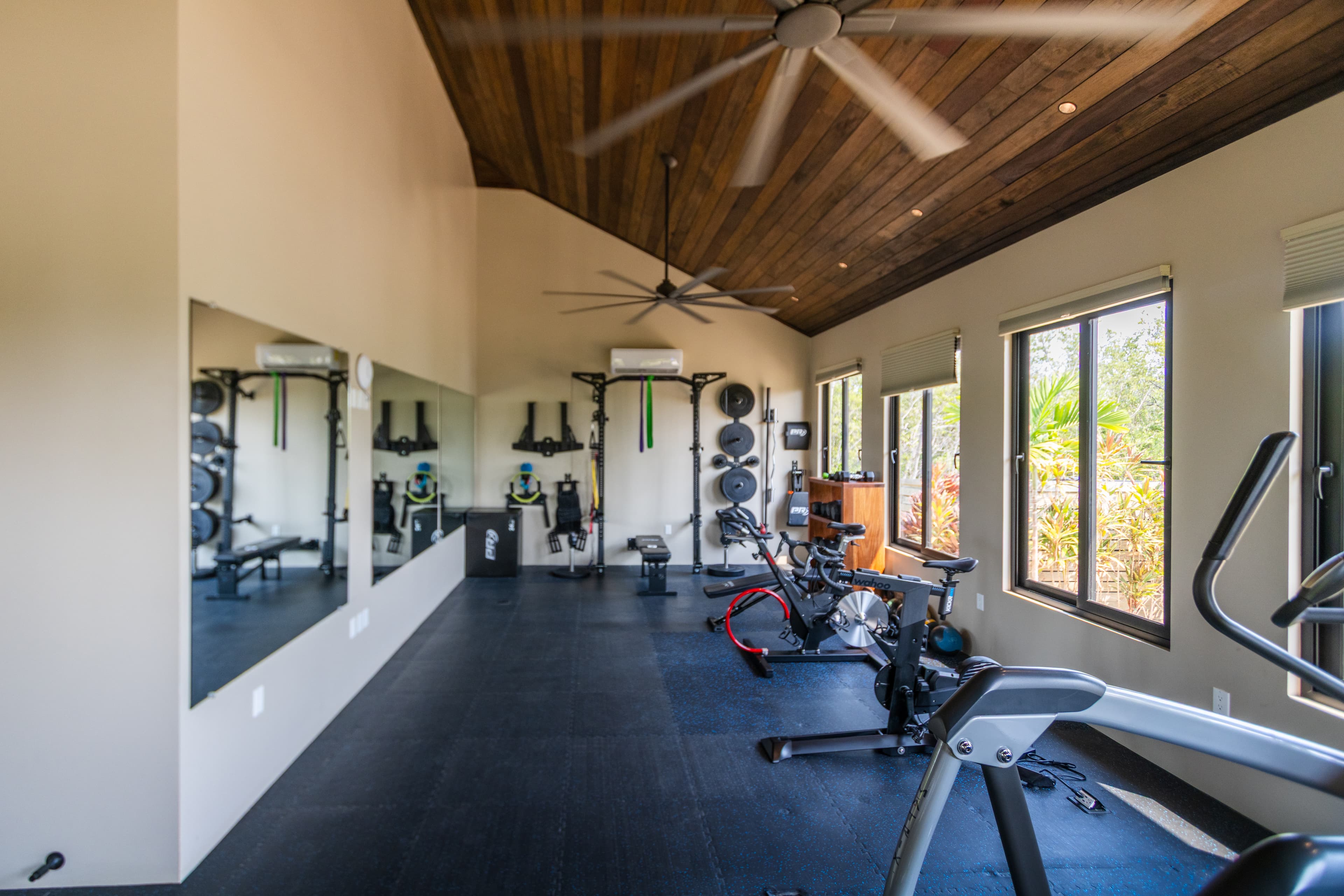 A modern home gym featuring exercise equipment, large mirrors, and windows for natural light.