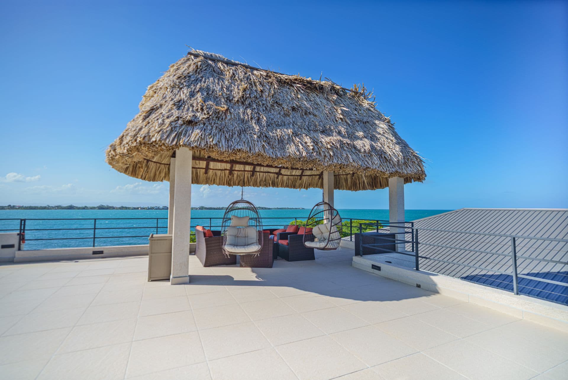 A thatched-roof gazebo overlooks a tranquil sea, featuring cozy seating underneath.